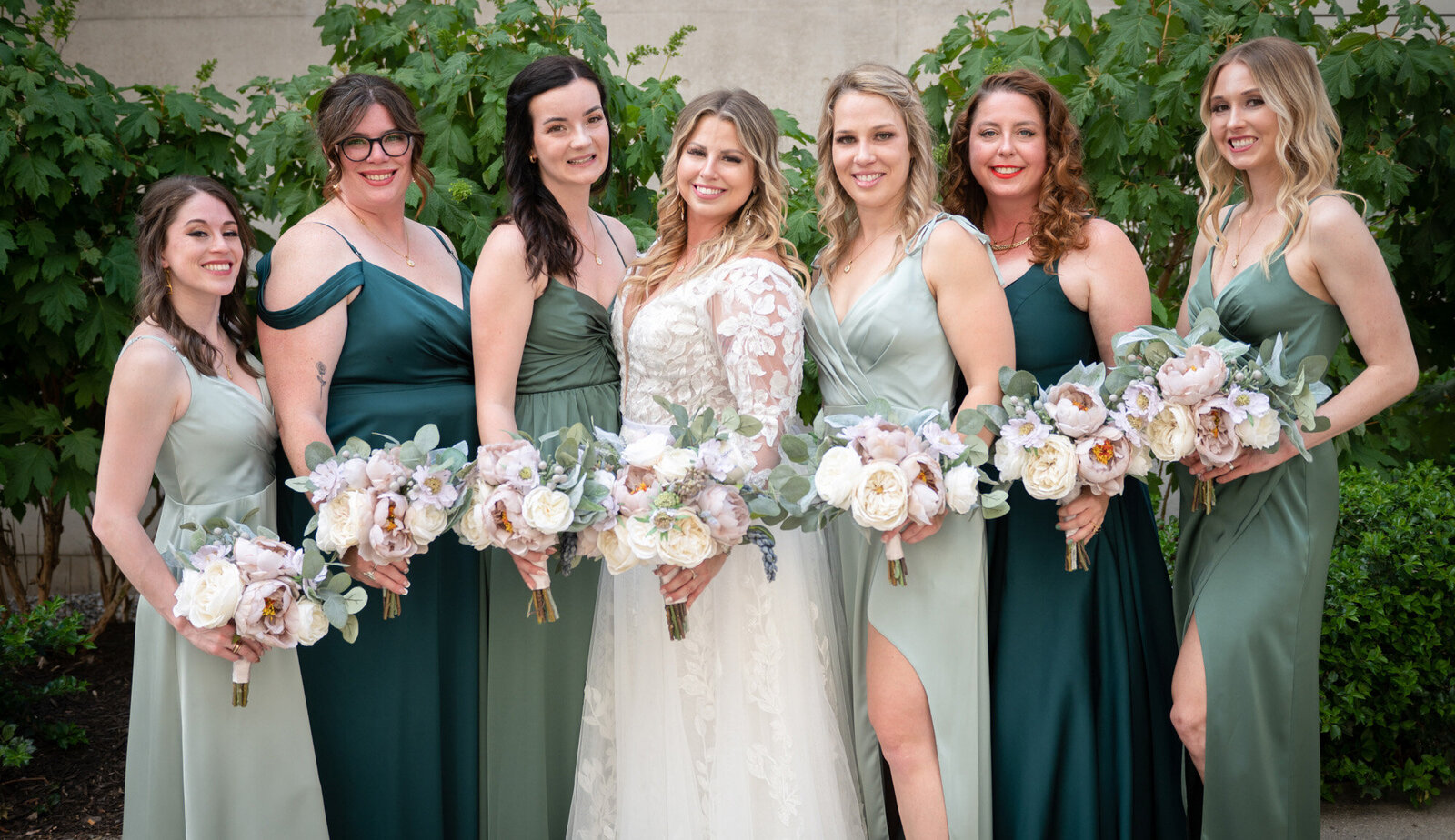bride and bridesmaids in green dresses pose with flowers