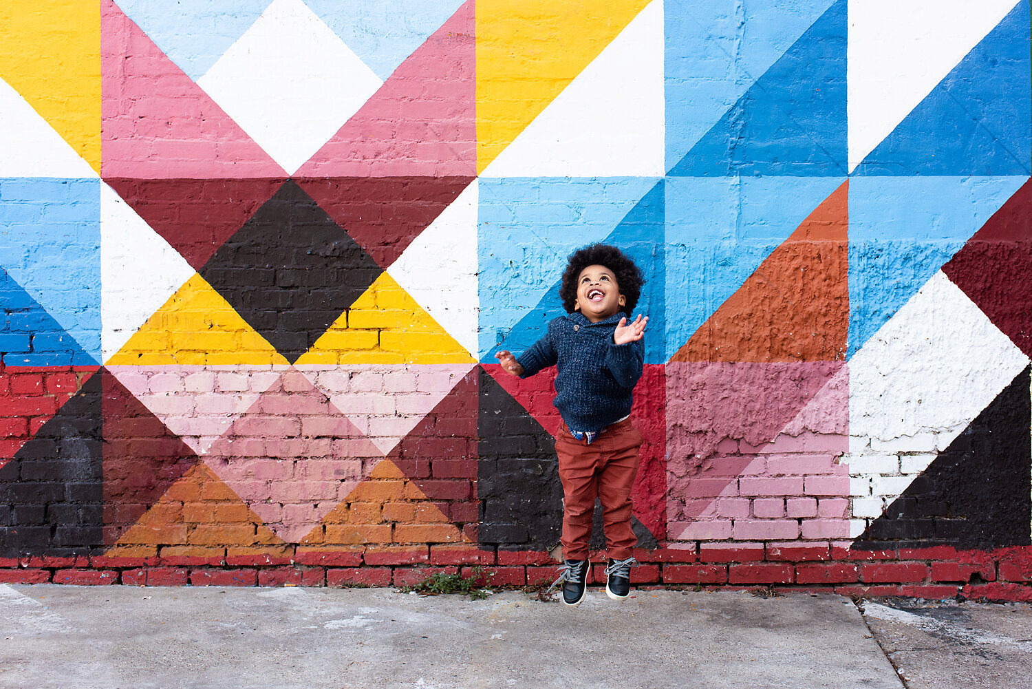 Young boy jumping in the air in front of a colorful brick wall at his family photo shoot in Deep Ellum, TX
