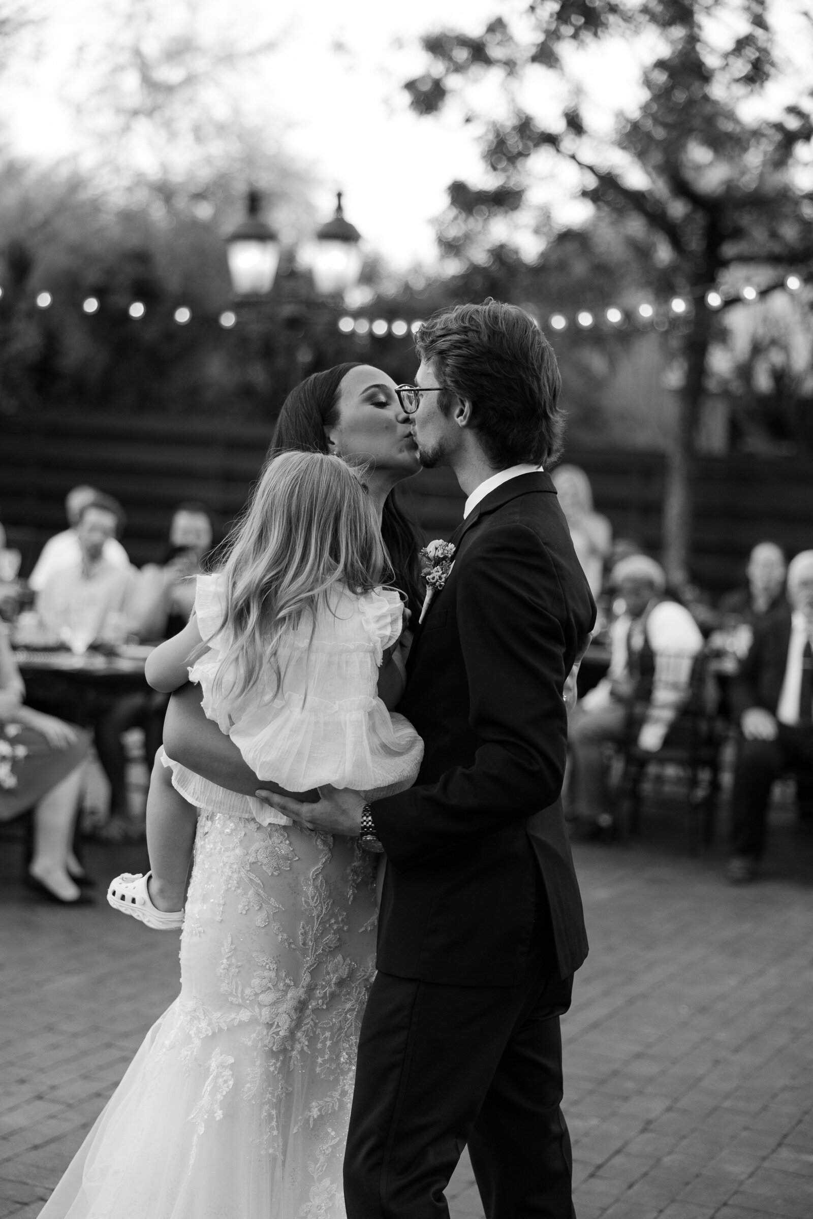 A bride and groom kissing while they hold a small child.