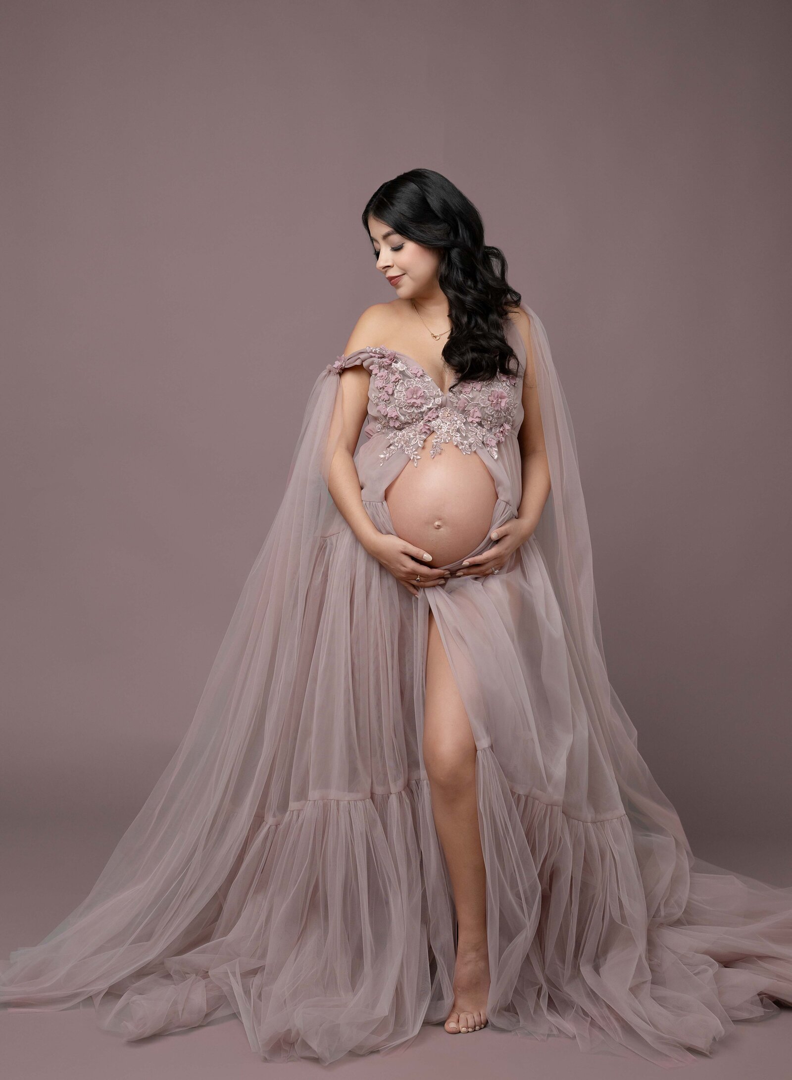 Mom wearing high end maternity gown and holding baby bump while looking over shoulder. Maternity portrait taken by Jenni. Nikki Photography at Atlanta Photo Studio. 