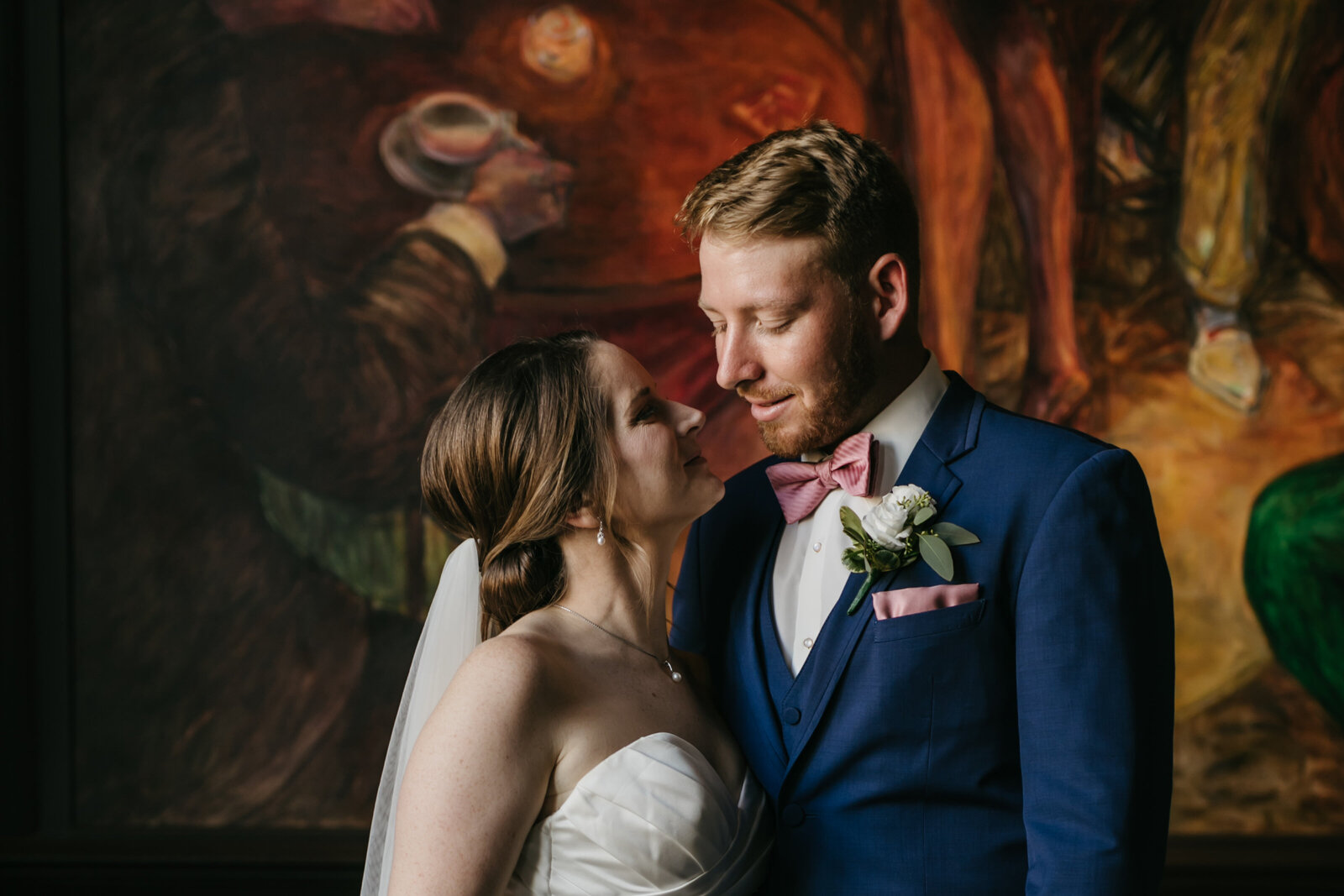 A bride and groom stand together in front of a colorful painting