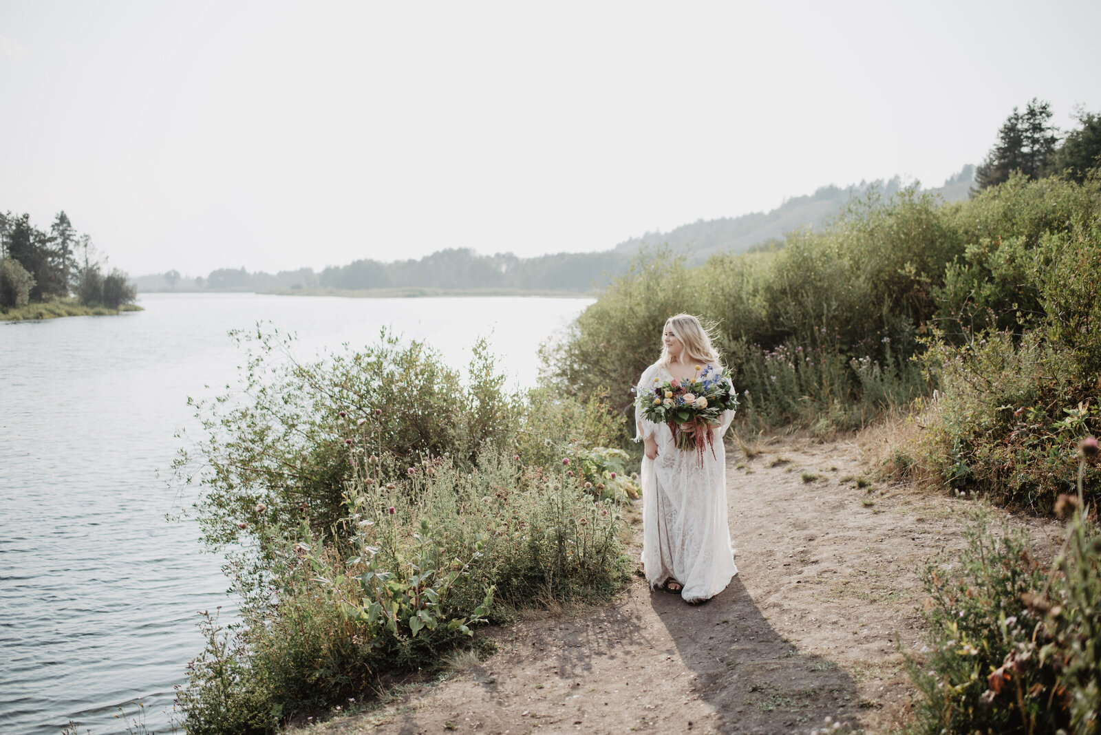 bridal portrITS FOR jackson hole wedding  with a young blonde bride holding and large floral bouquet and looking out into a river for her spring wedding in the grand tetons