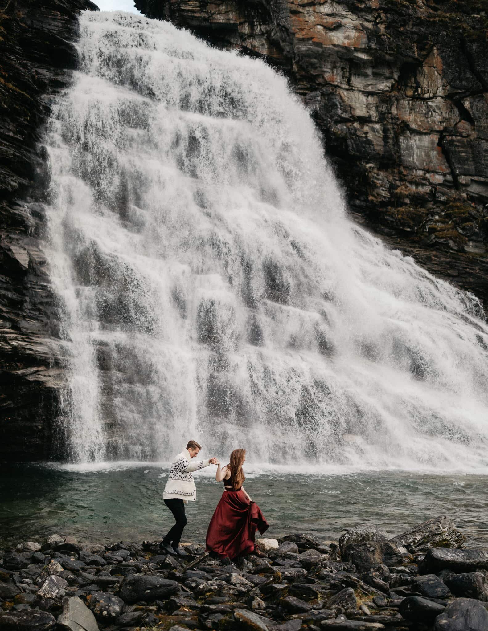 Couple walking in front of waterfall in Norway
