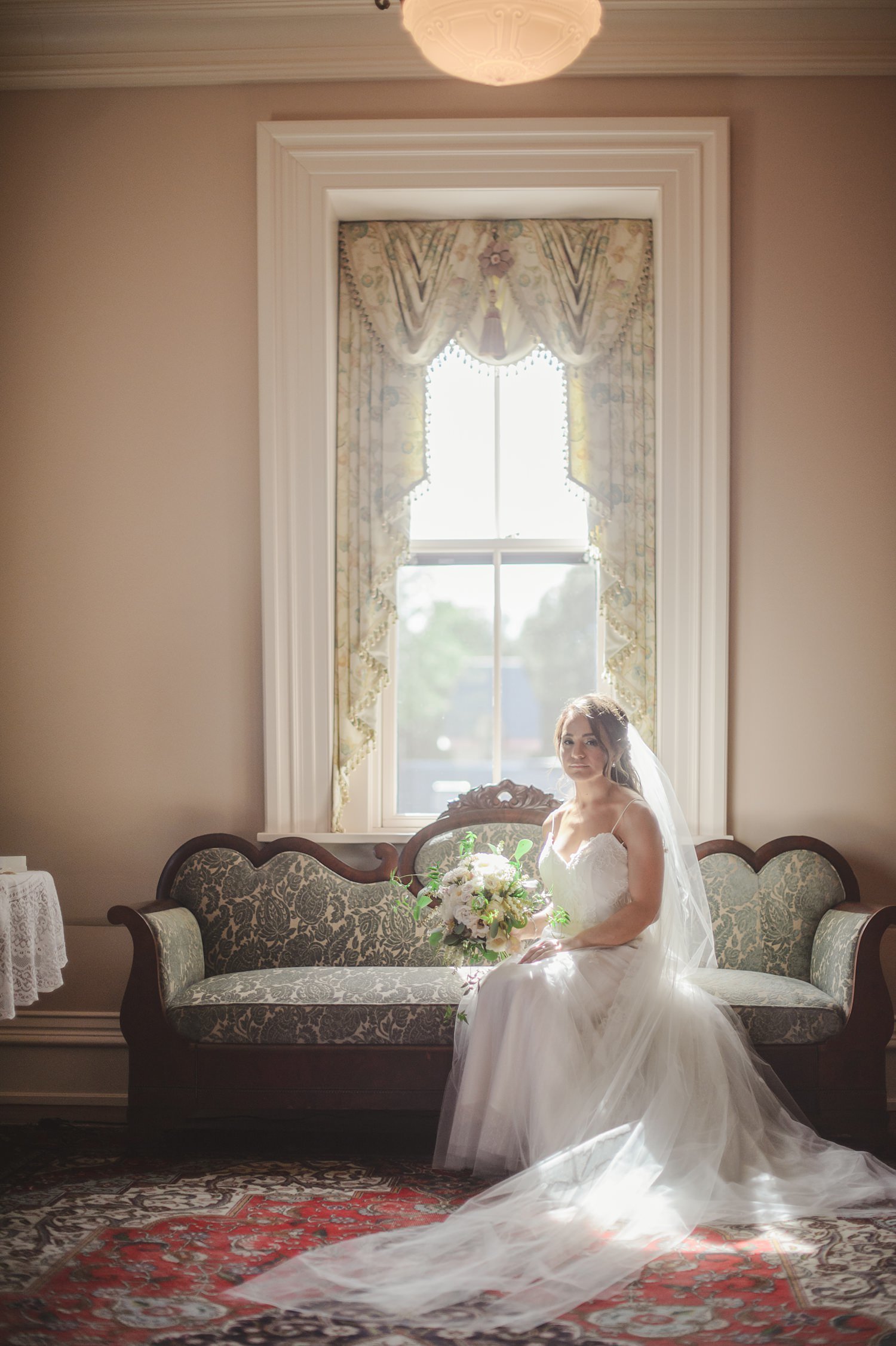 Bride next to window on vintage sofa at The Webb Barn in Wethersfiled, CT