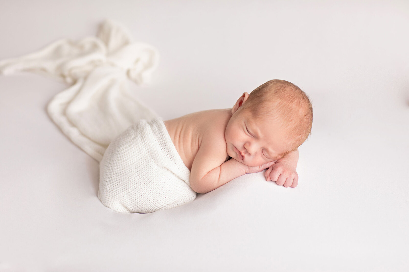 a sleeping newborn wrapped at the waist with a soft white cloth with a hand under their cheek, taken by Ivory Tree Portraits.