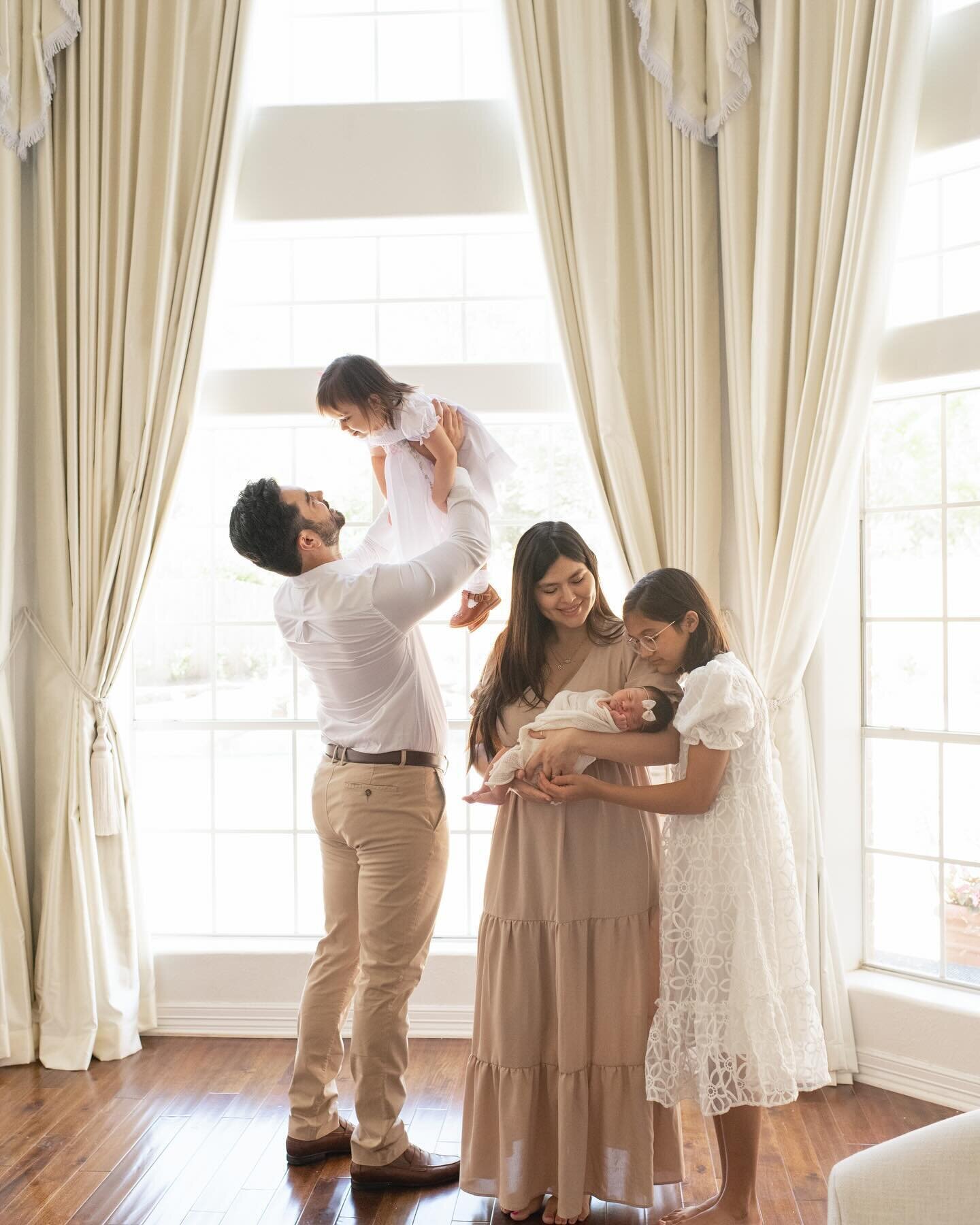 Parents and two children stand by a bright window, holding hands. A light-filled lifestyle family session by Moments in Light Photography.