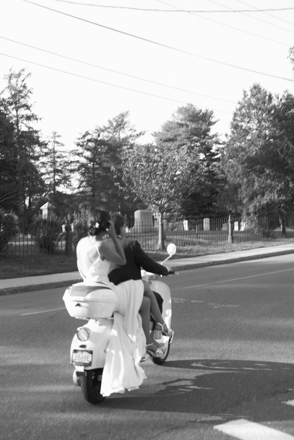 Bride and groom riding away on a scooter together