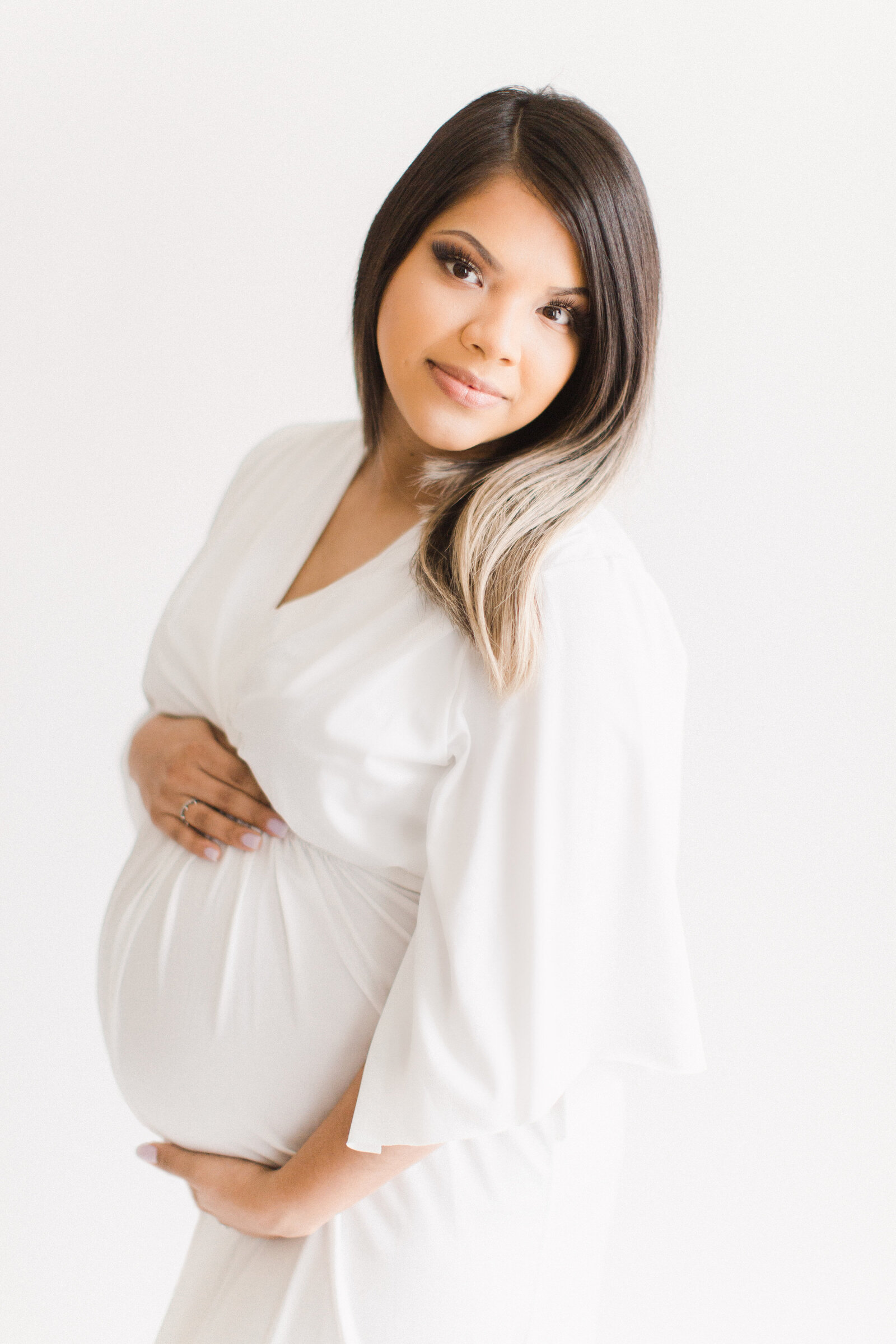 Mom in white dress on white background studio maternity photo.