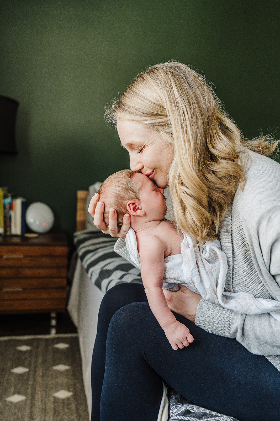 mom holds babys head to lips in green bedroom