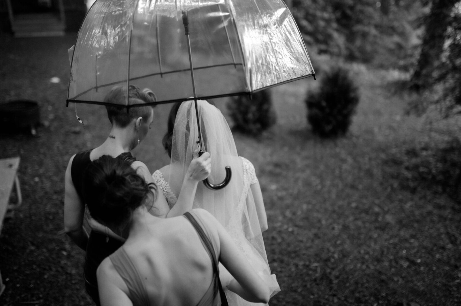 bride and bridesmaids walking outside with clear umbrella rainy wedding