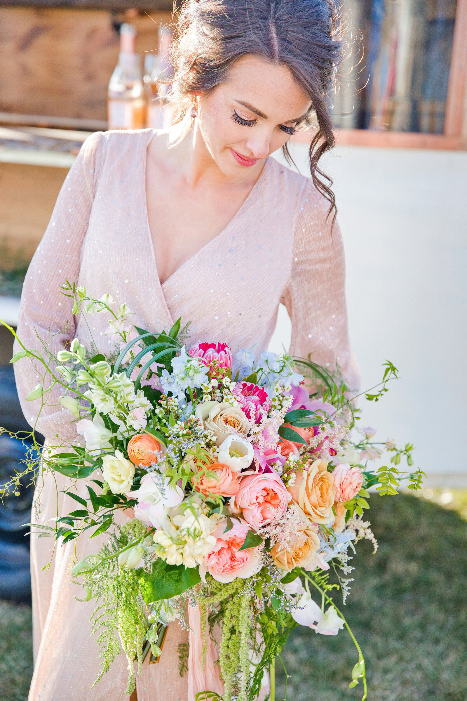 Bride standing in a pale pink dress holding her wedding bouquet looking down at it.