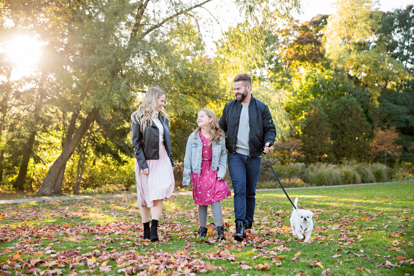 family with small white dog walking fall with leaves on ground