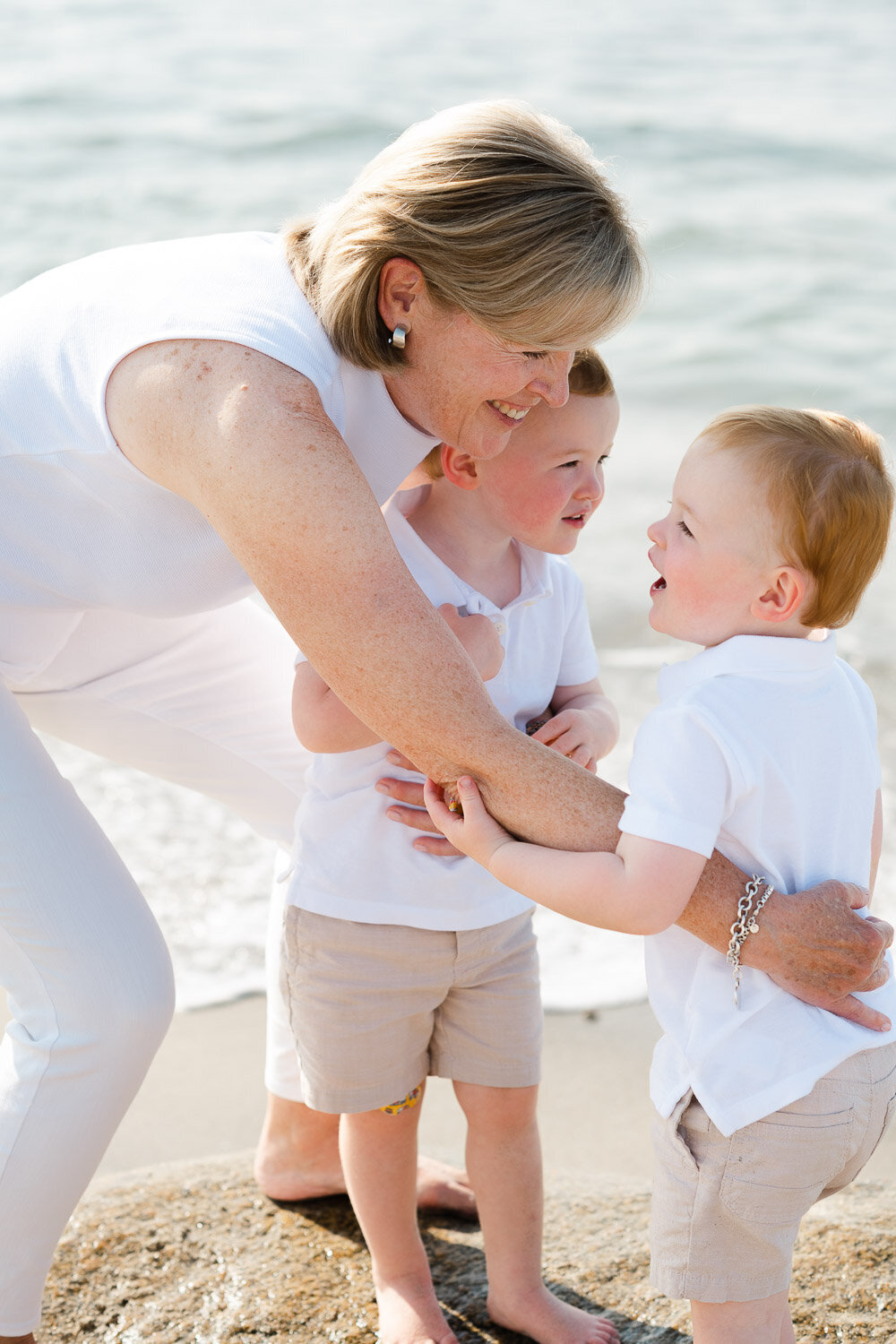 grandma smiles and hugs twin grandsons on beach