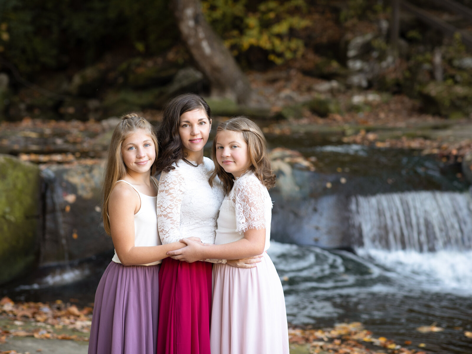 mother and two daughters standing by waterfall for family photos