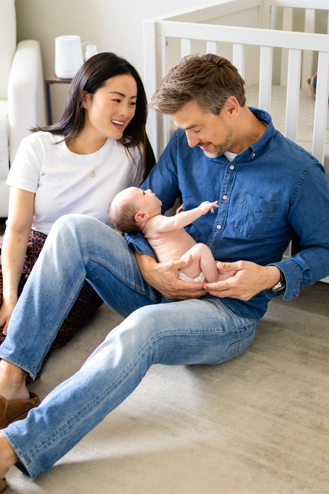 Parents lovingly gaze at their newborn baby during an in-home lifestyle session in a softly lit nursery — Ellobelle Photography Family Photographer.