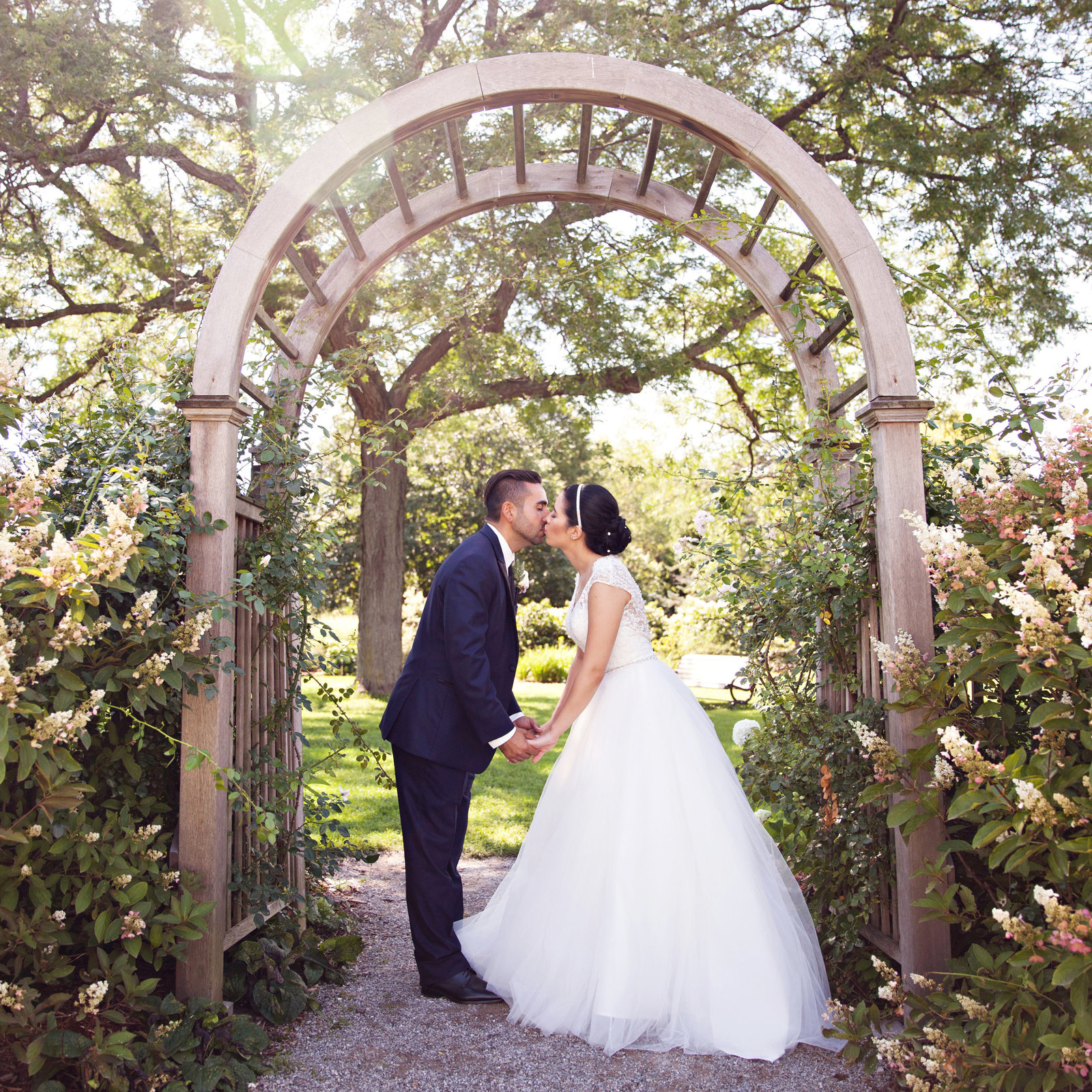 bride and groom kissing under arch with bushes and flowers at Royal Botanical Gardens in Burlington