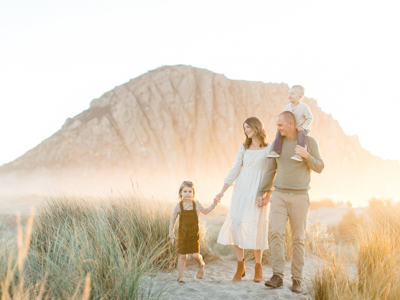 family of four walking together in the sand by a rock hill