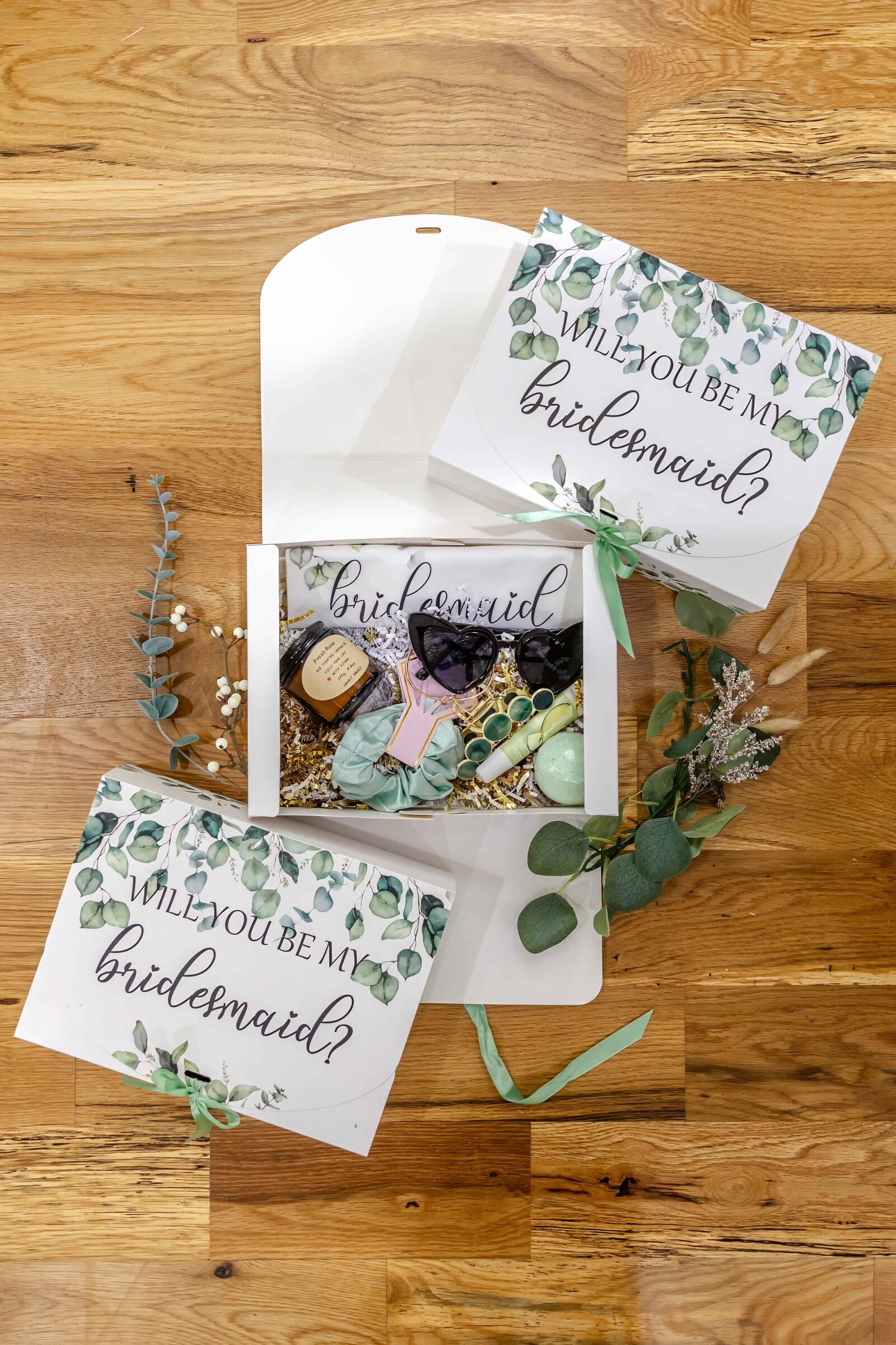 Elegant bridesmaid proposal boxes with greenery-themed designs and thoughtful gifts, captured at a Wilmington, NC wedding, showcasing creative and personalized wedding details.