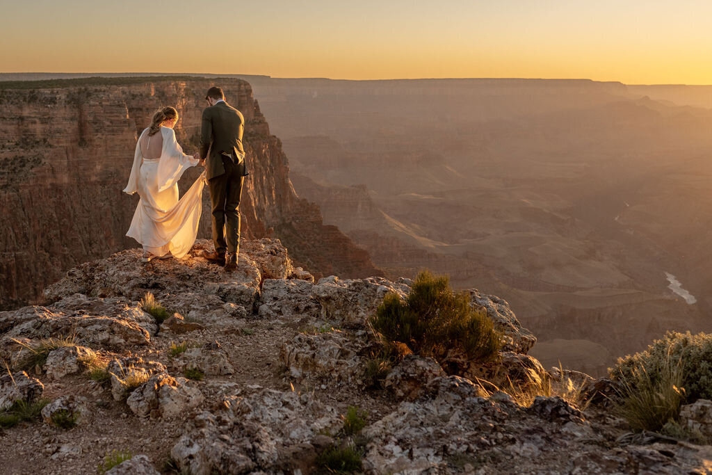 A couple sharing a private wedding ceremony at the South Rim of the Grand Canyon with dramatic red rock cliffs behind them.