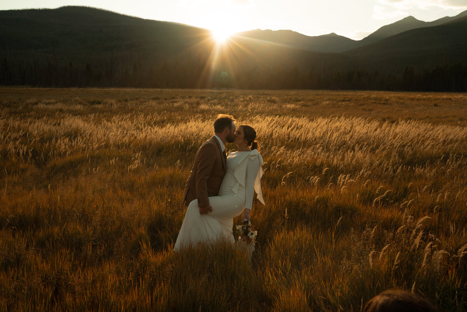 A married couple kissing with the sunset behind them at their Rocky Mountain National Park elopement.