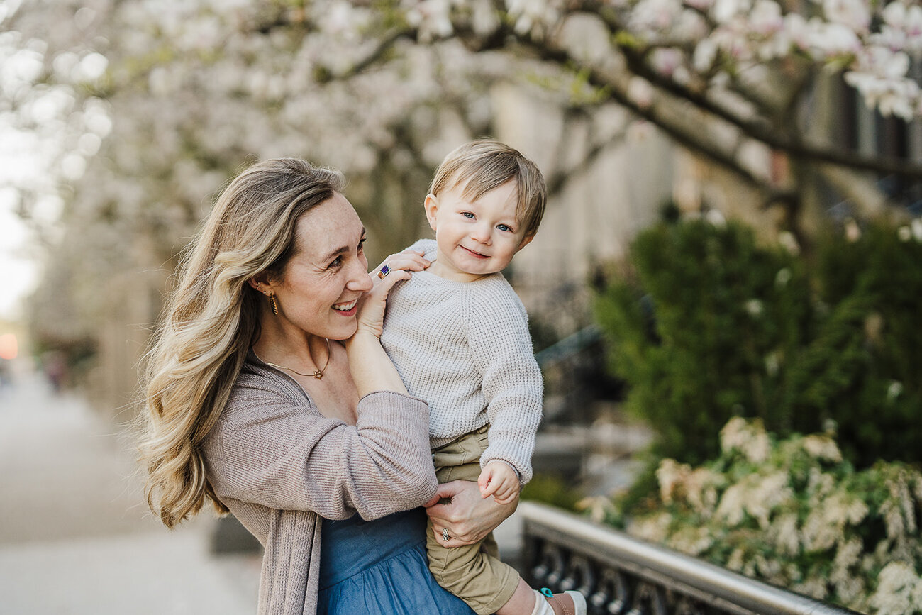 mother tickles son under chin in front of magnolia tree in boston