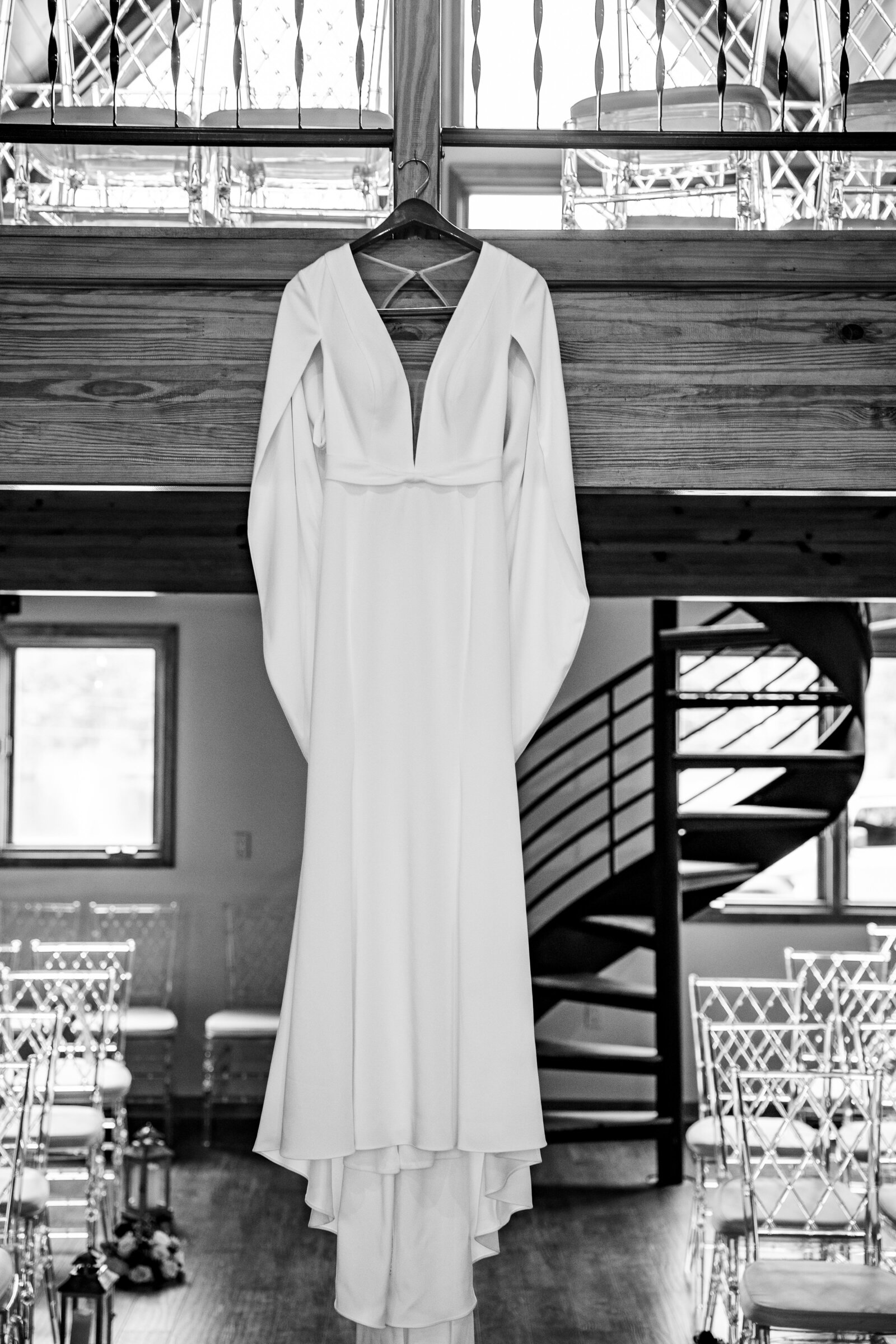 Black and white shot of wedding dress hanging from the balcony in the ceremony room at Kincaid Manor, adding a timeless touch."