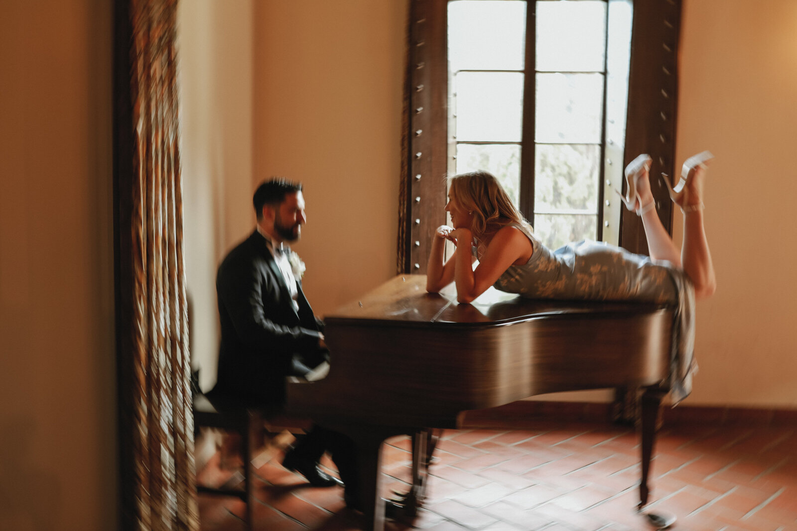 man sitting at grand piano while woman lays on top of grand piano and smiles at the man