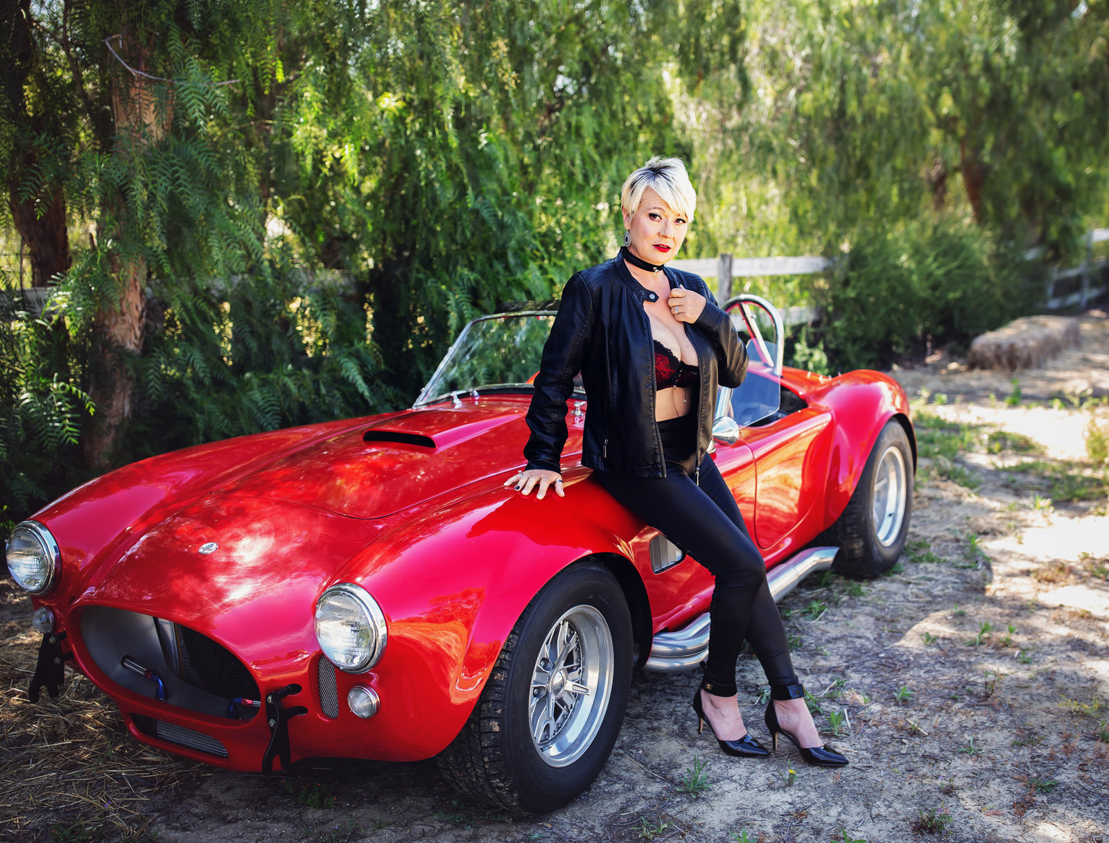 Woman wearing black boudoir suit sitting on red sports car
