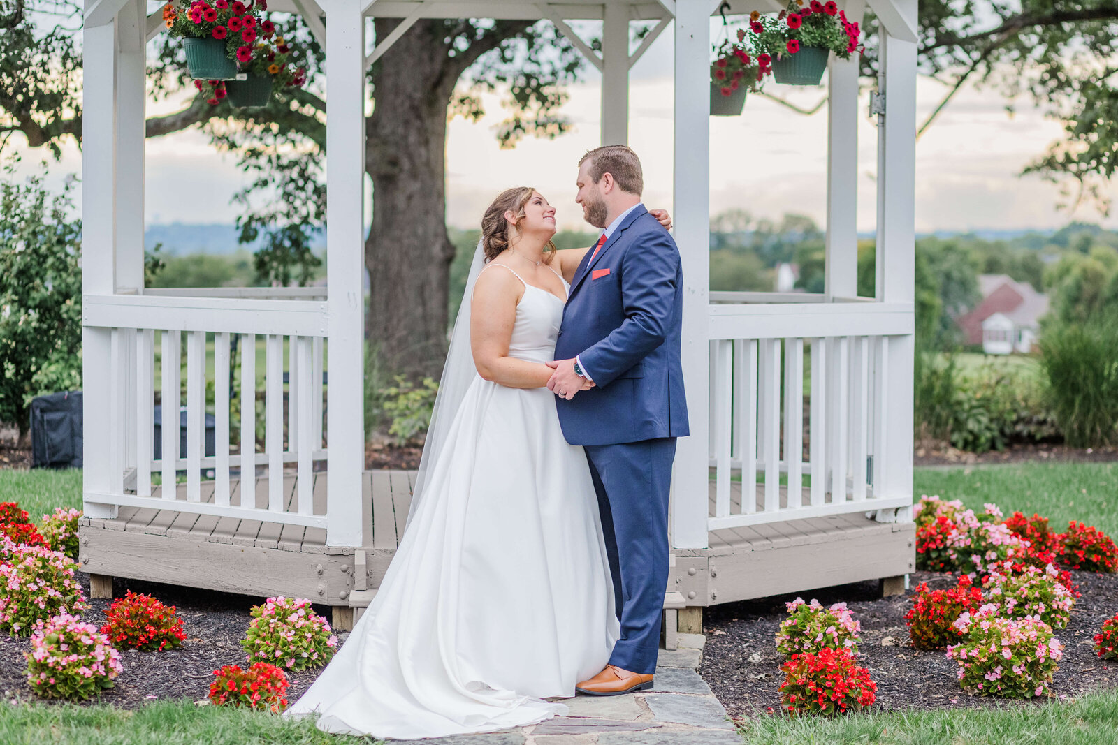 bride and groom stand looking at each other as they stand in front of gazaebo at walden ponds surrounded by many flowers. taken by cincinnati ohio wedding photographer