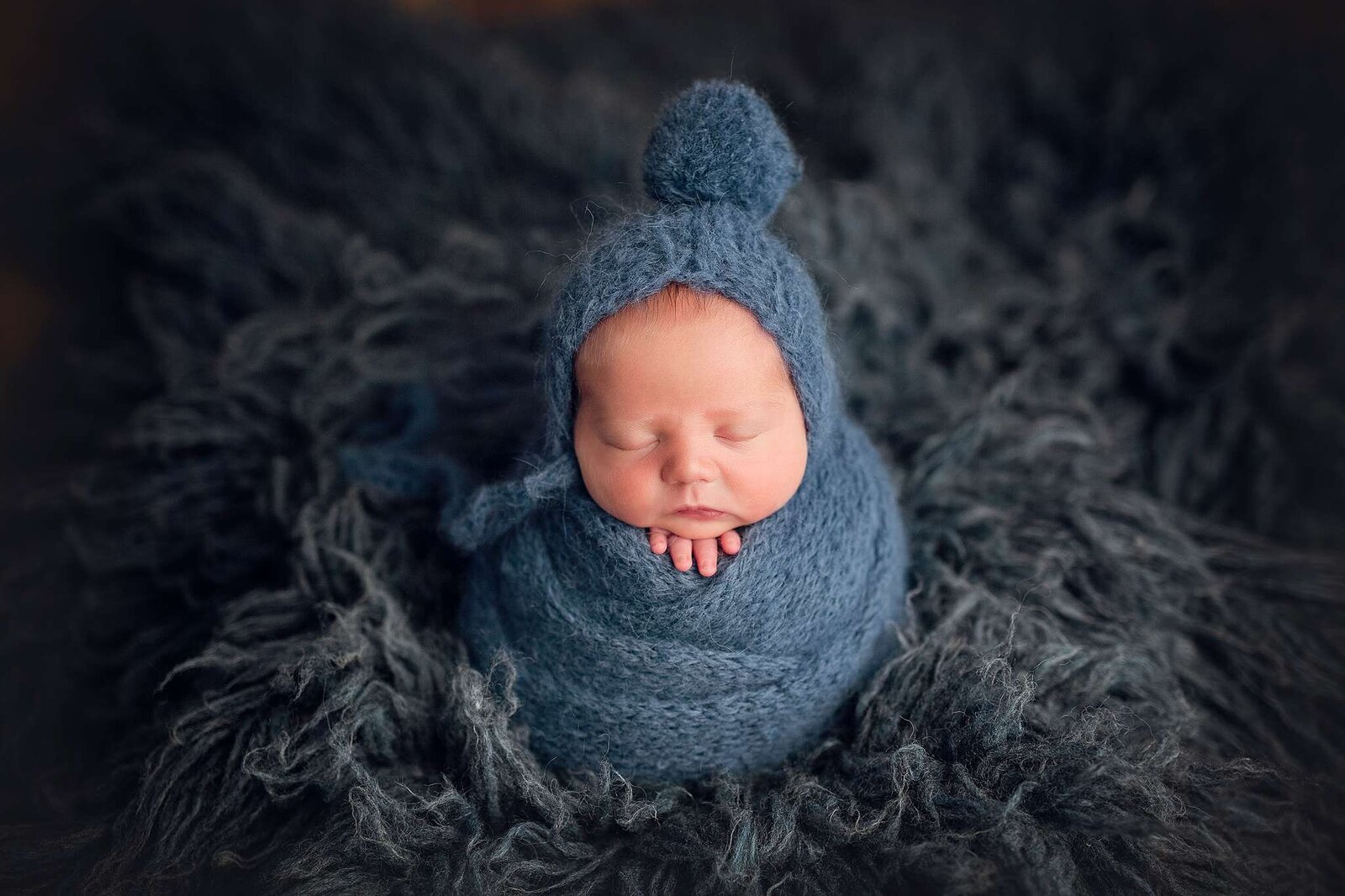 A newborn boy in a blue knitted hat, photographed by Bia Schaefer during an in-home session in Orlando.