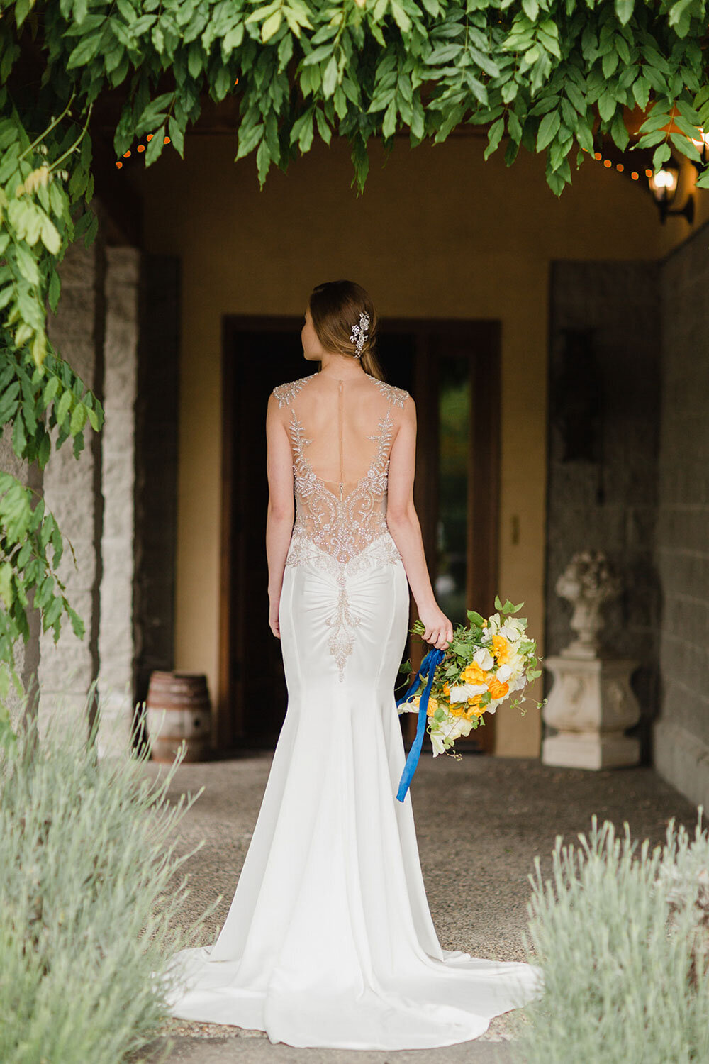 Bride standing under lush greenery holding a colorful bouquet