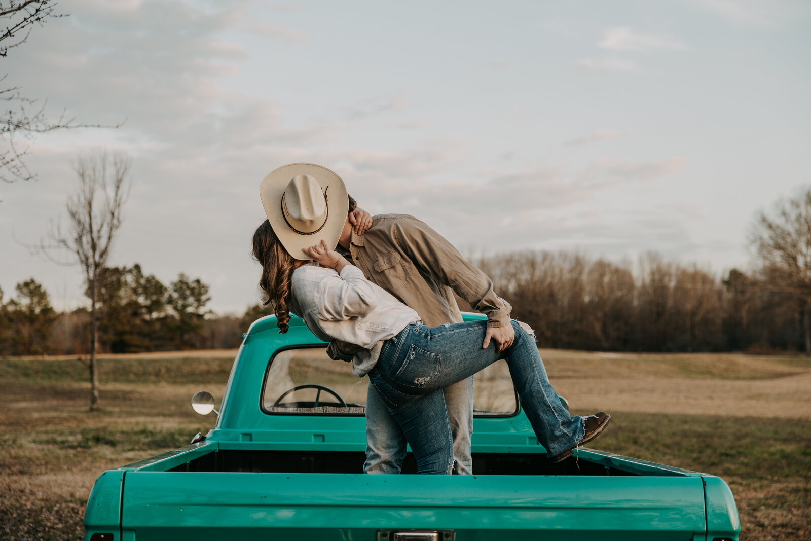 Jacob dips Laura down in the bed of a vintage truck, his cowboy hat in front of their faces as they share a kiss.