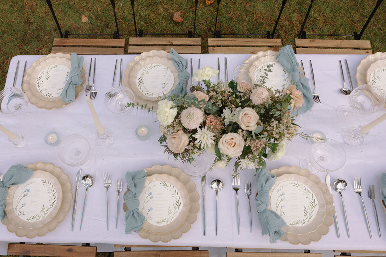 Outdoor tablescape with blue linens, floral centerpiece, and candles