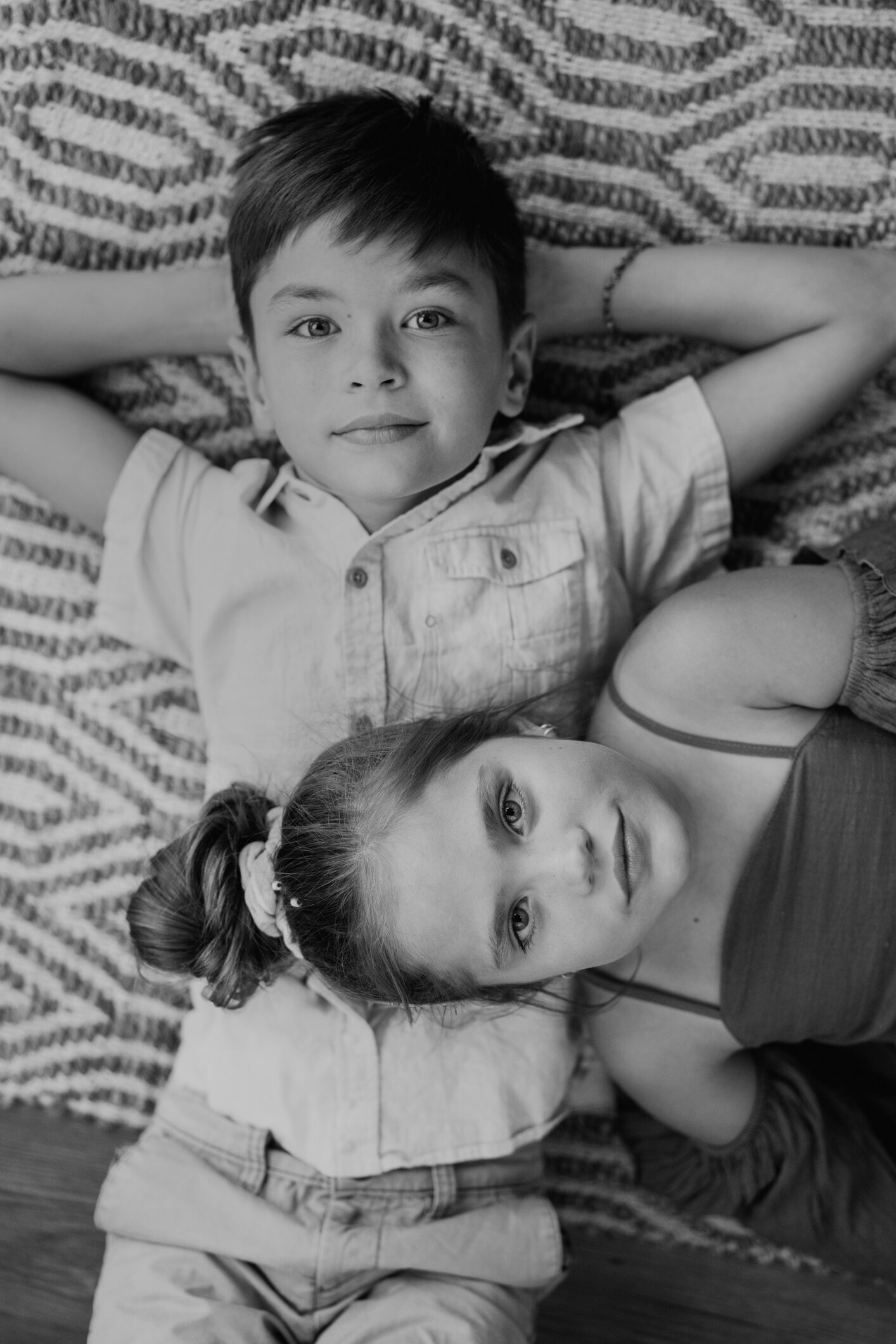 A brother and sister lay on the floor with their heads close together, making direct eye contact with the audience while wearing Boho clothing.