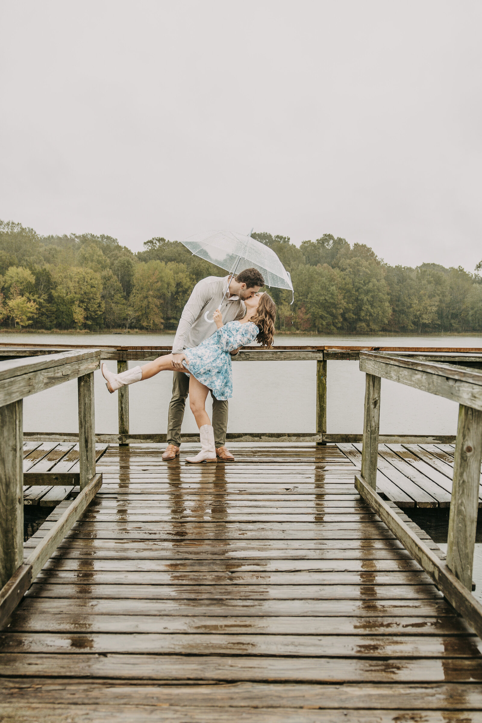 Drake kissing Lauren in a romantic dip on a dock during their rainy day engagement session at Shelby Farms Park.