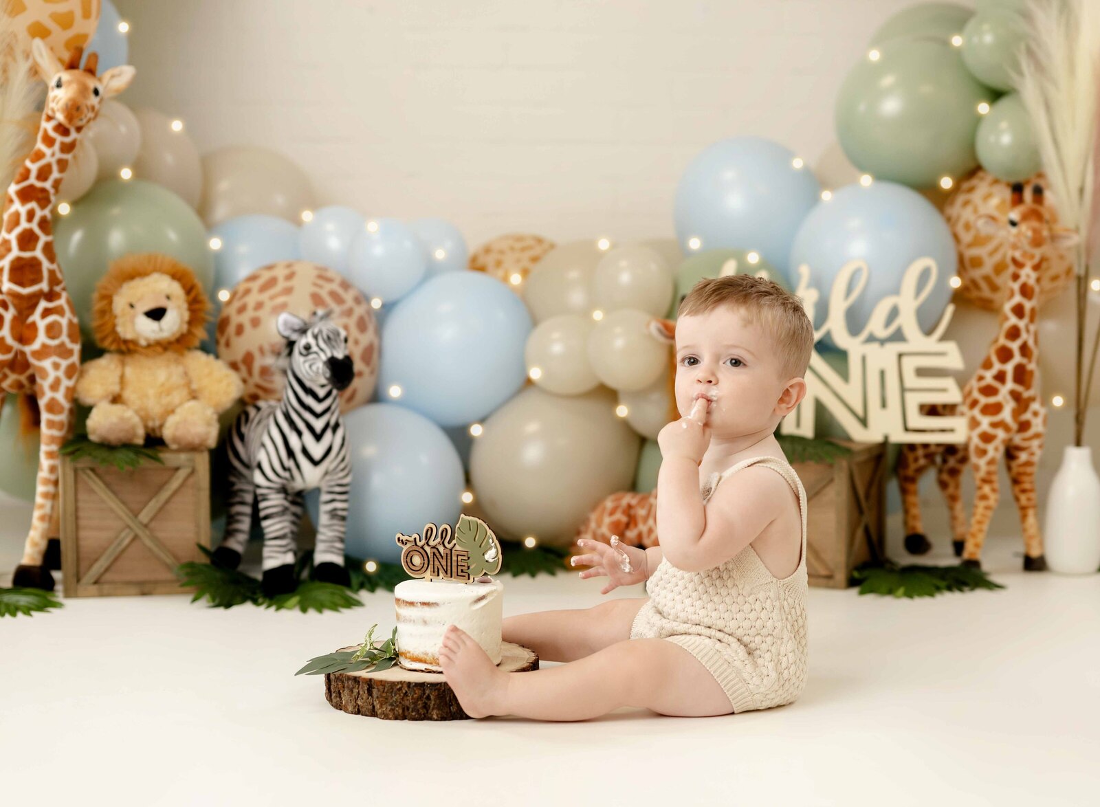 Baby licking his finger, eating cake for Safari themed cake smash set. Photographed at Atlanta baby studio.