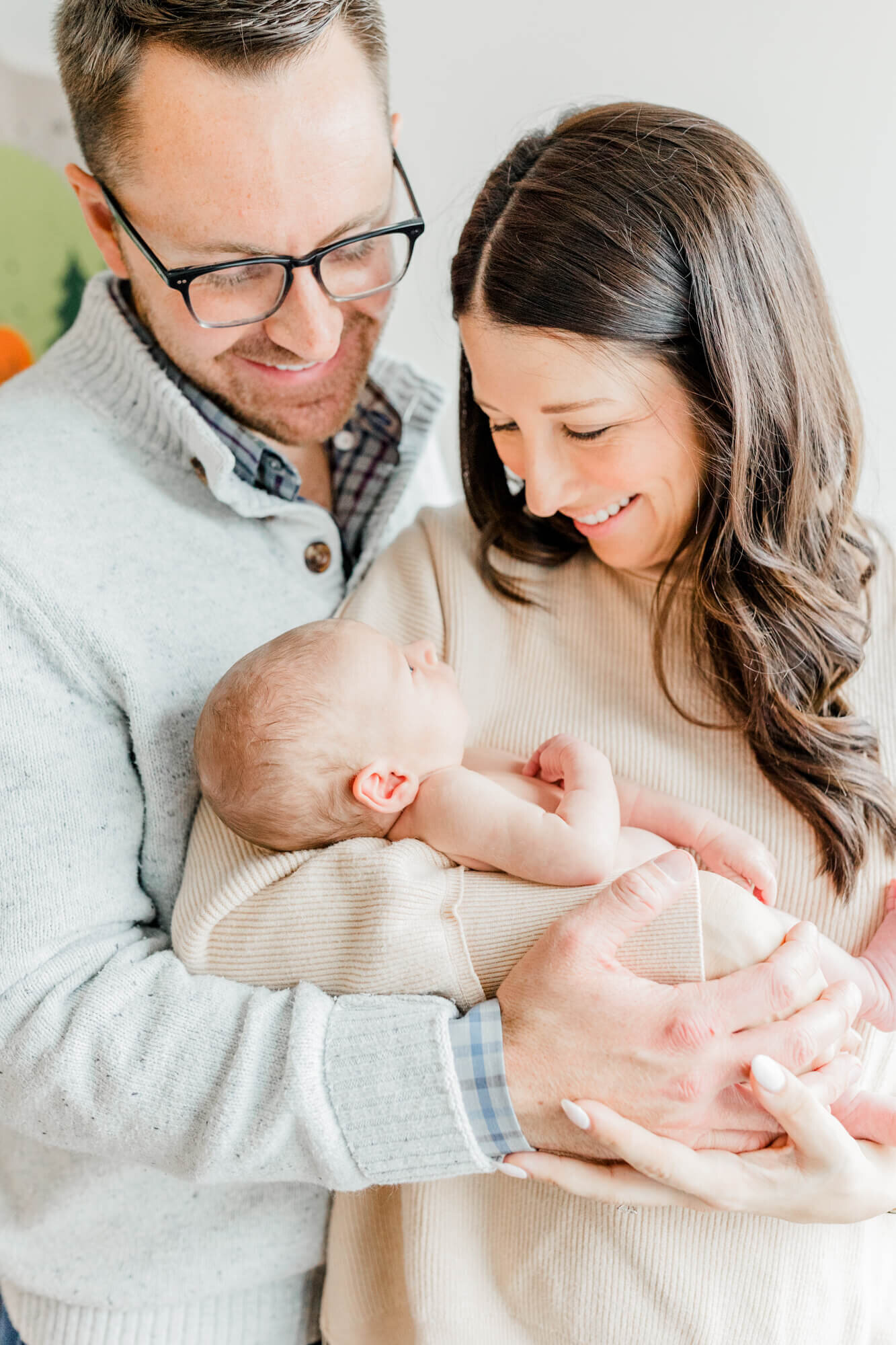 Mom and dad smile at their newborn at a session by a Boston Newborn Photographer