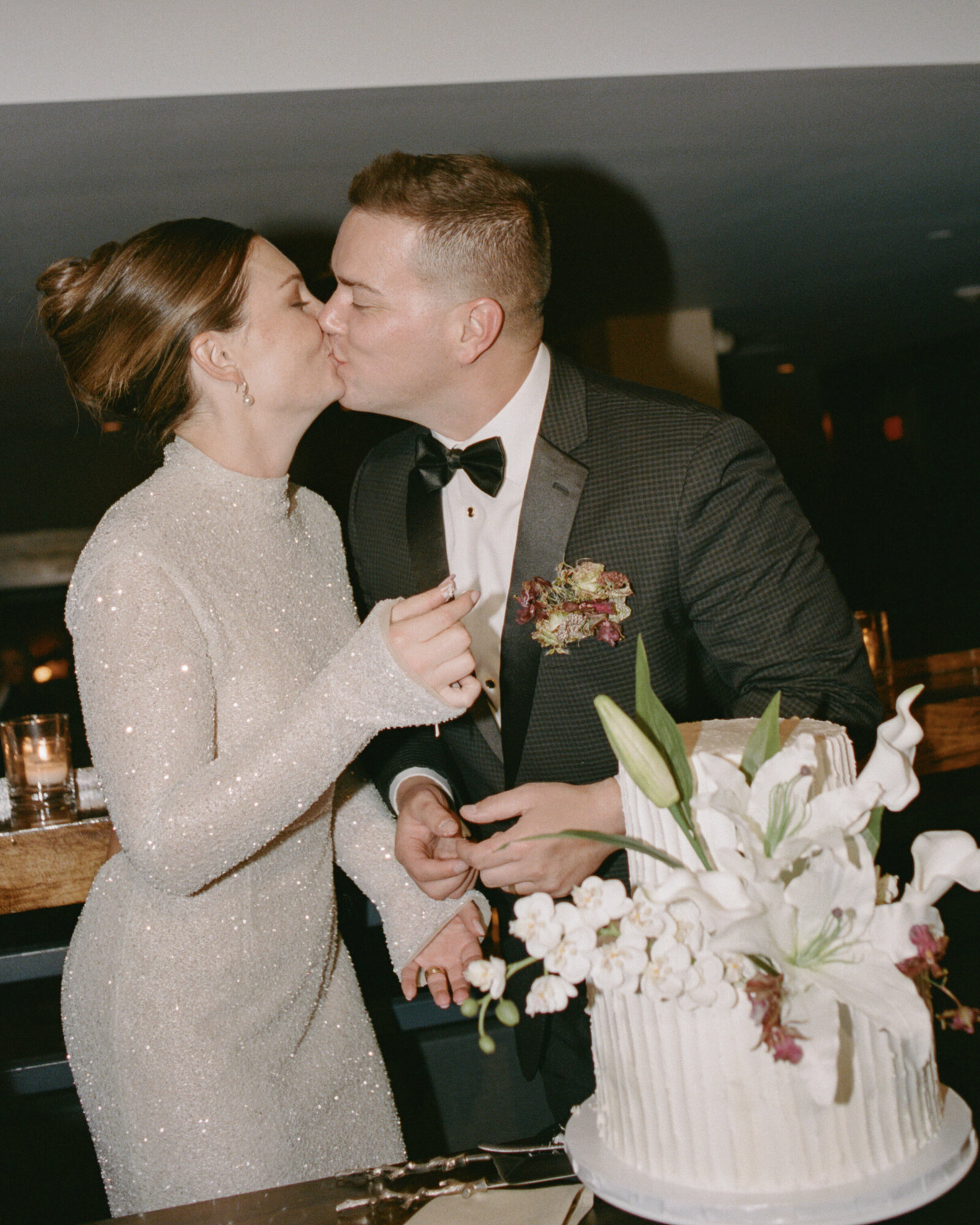 Direct flash film photo of bride and groom kissing at cake cutting with vintage style two-tiered cake with calla lily floral decorations