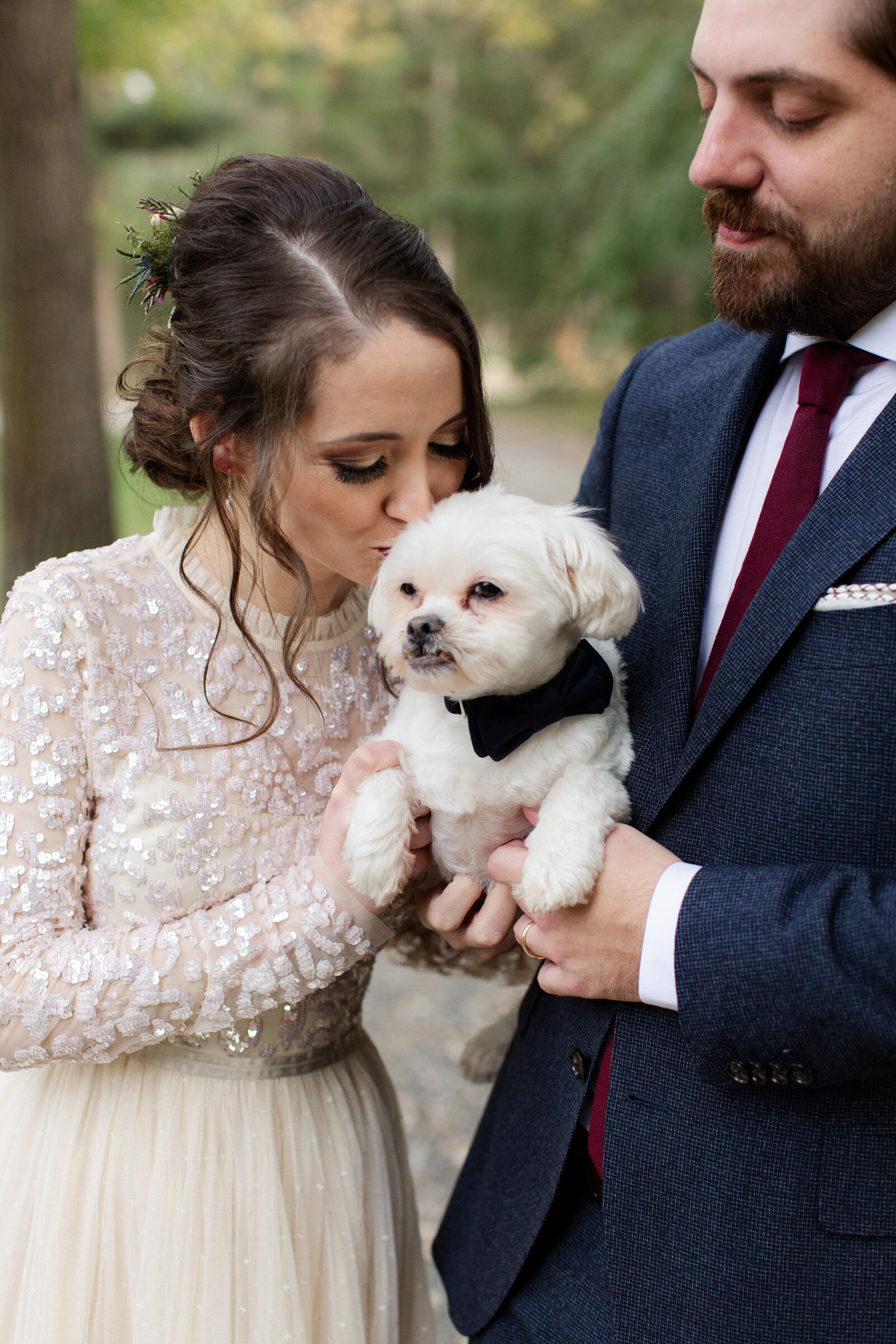 bride kisses white dog in black bow tie