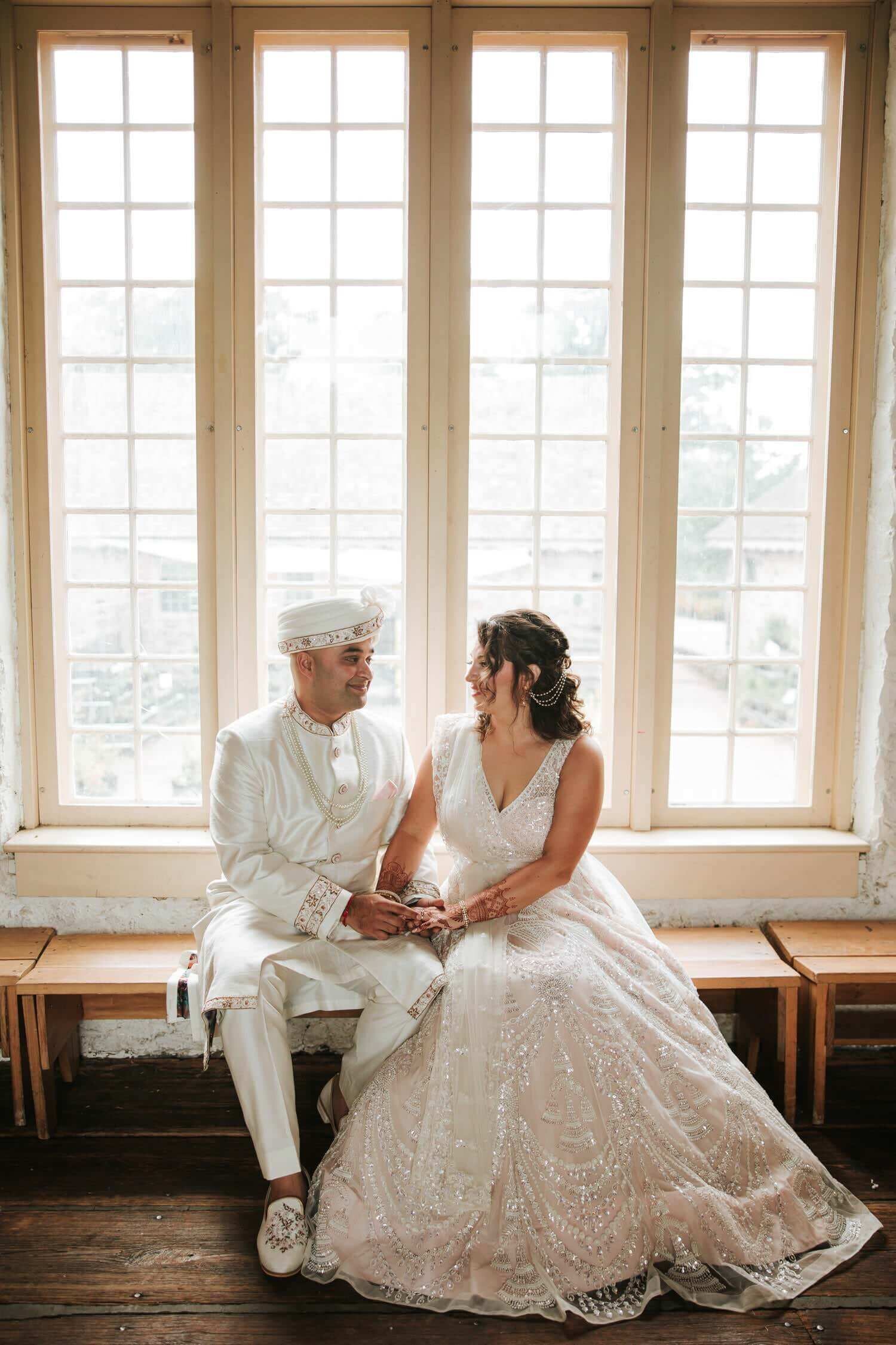 Bride and groom sitting by window  during portraits before ceremony