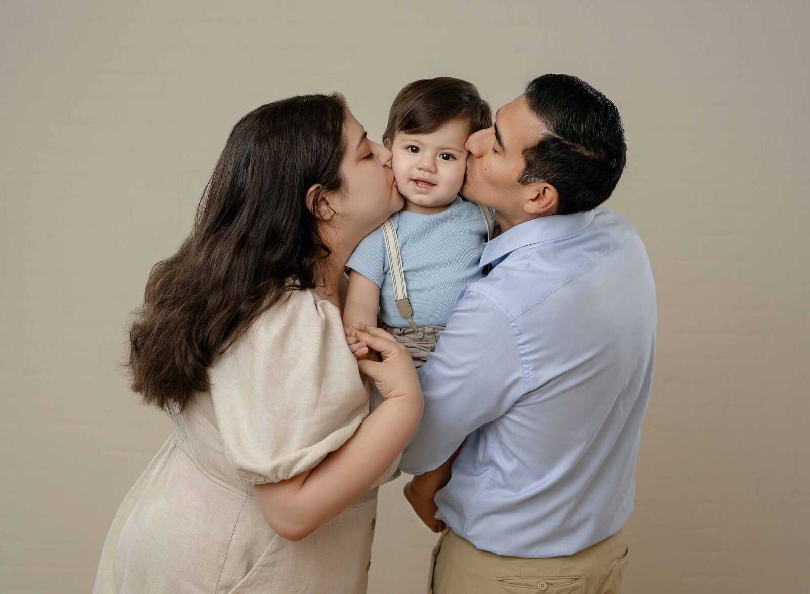 Mom and Dad holding baby in the middle and kissing his cheeks.