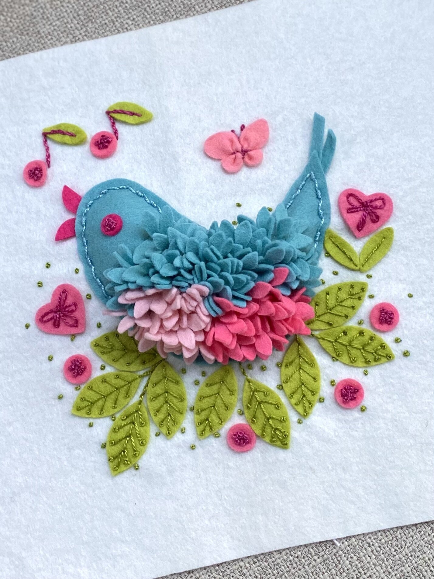 Song bird made out of felt with felt flowers and leaves.