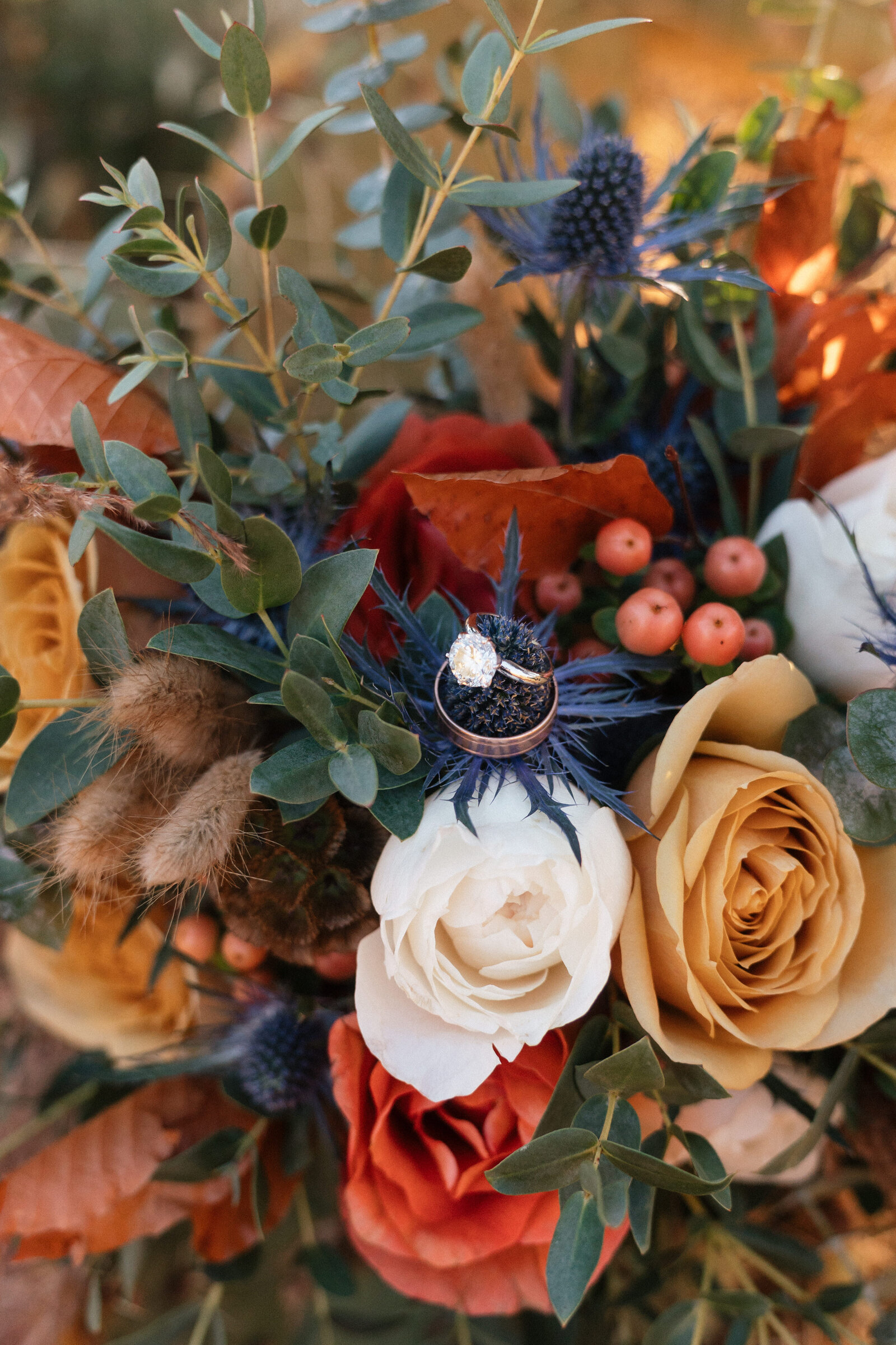 Close-up of wedding rings resting on a colorful bridal bouquet with roses, eucalyptus, berries, and thistle during an elopement at Merry Go Round Rock in Sedona, Arizona.