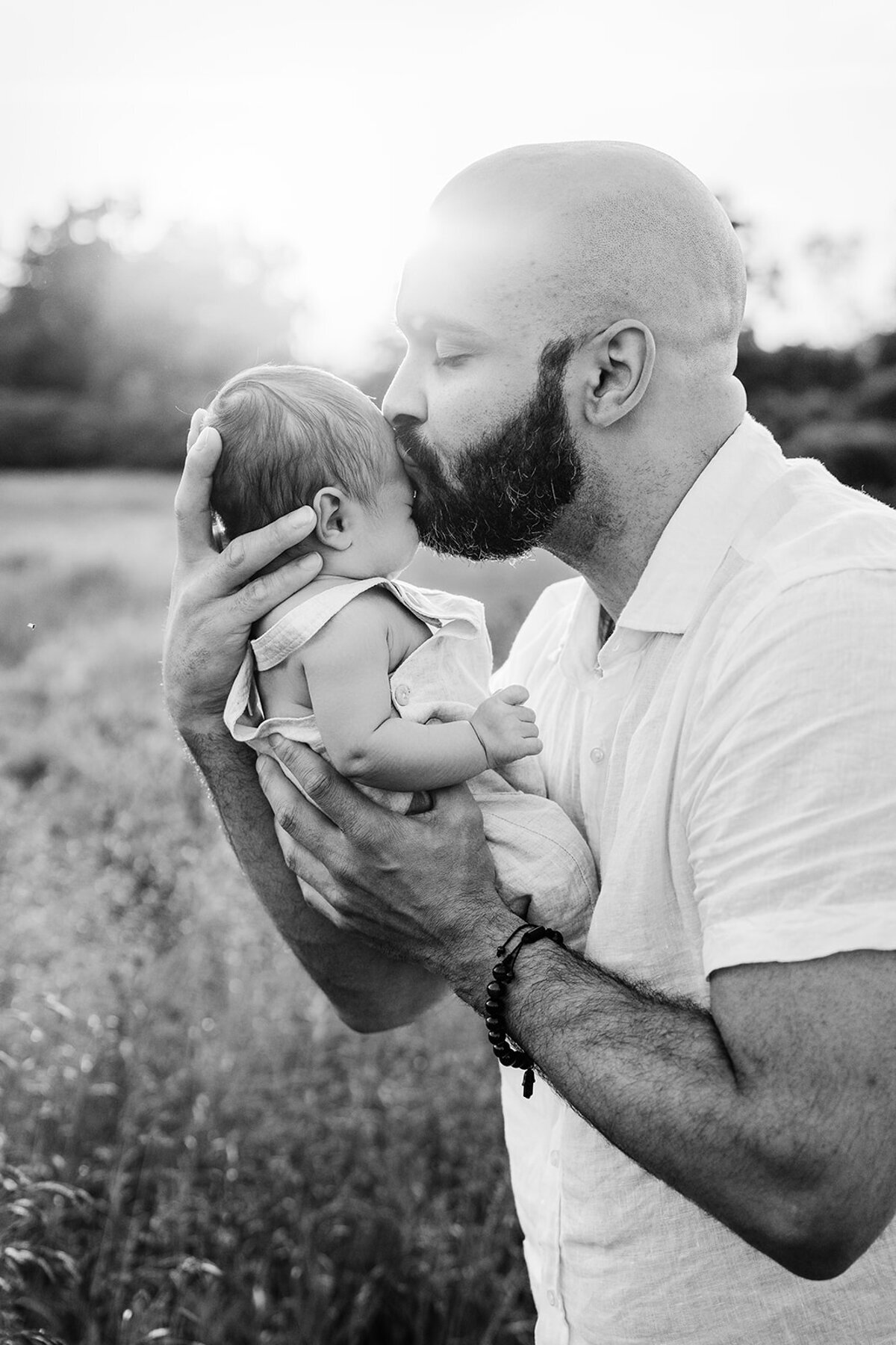 black and white portrait of a dad holding newborn boy outdoors at sunset