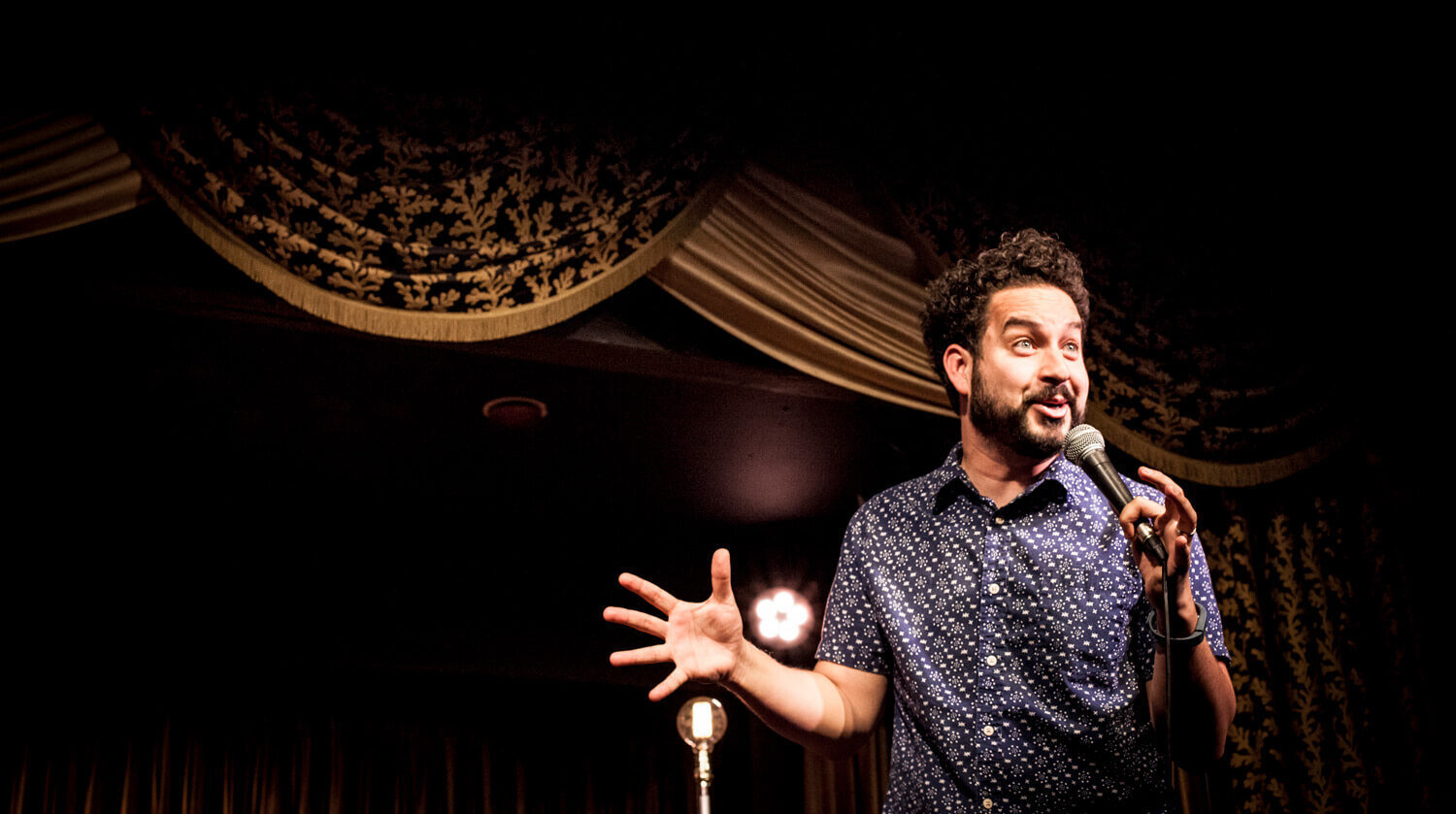 Ahmed Bharoocha holding a microphone and doing stand up comedy