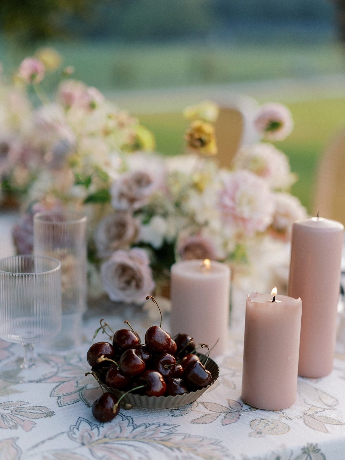 Blush candles lit beside a dish full and cherries and florals in the background.