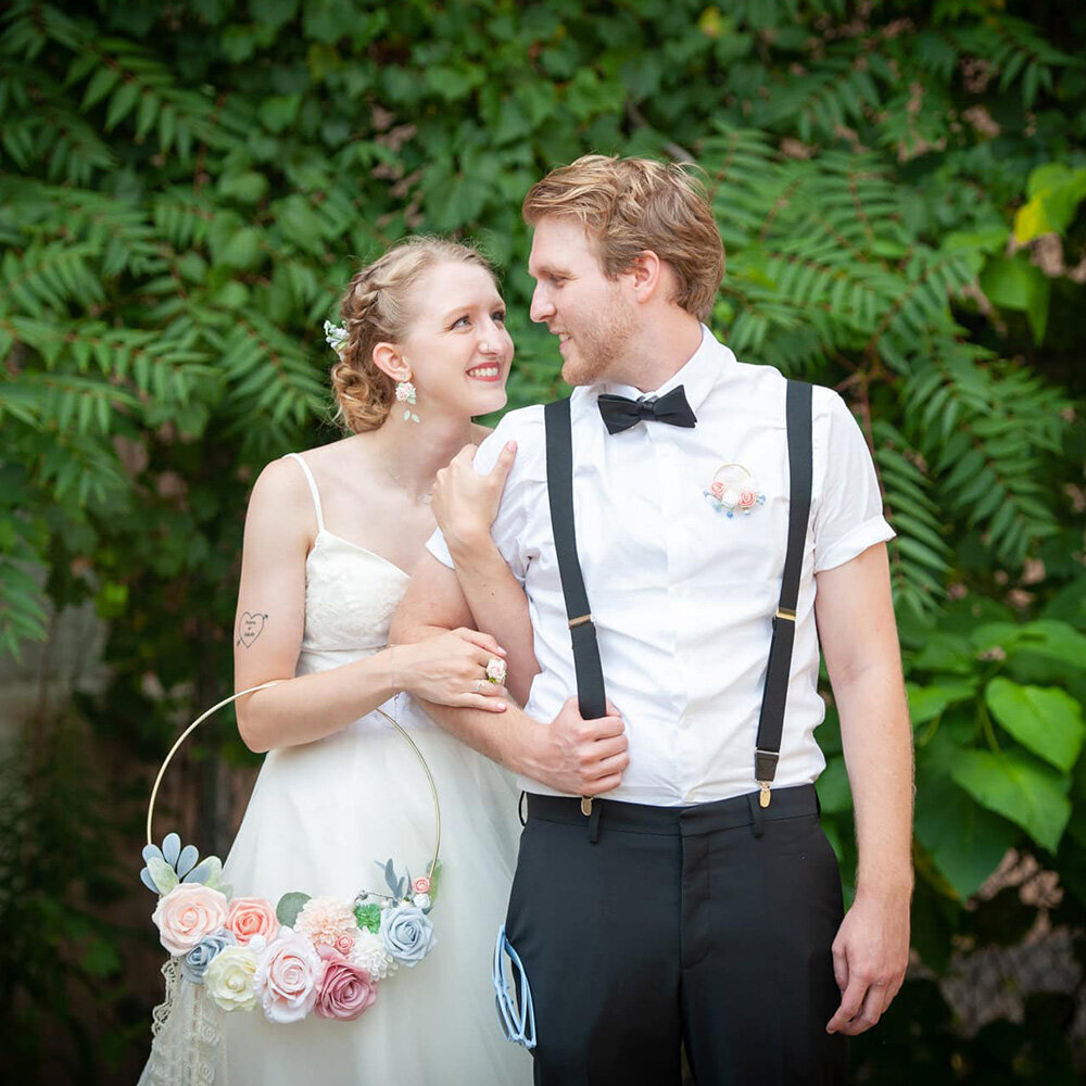 bride holds groom in suspenders smile at each other