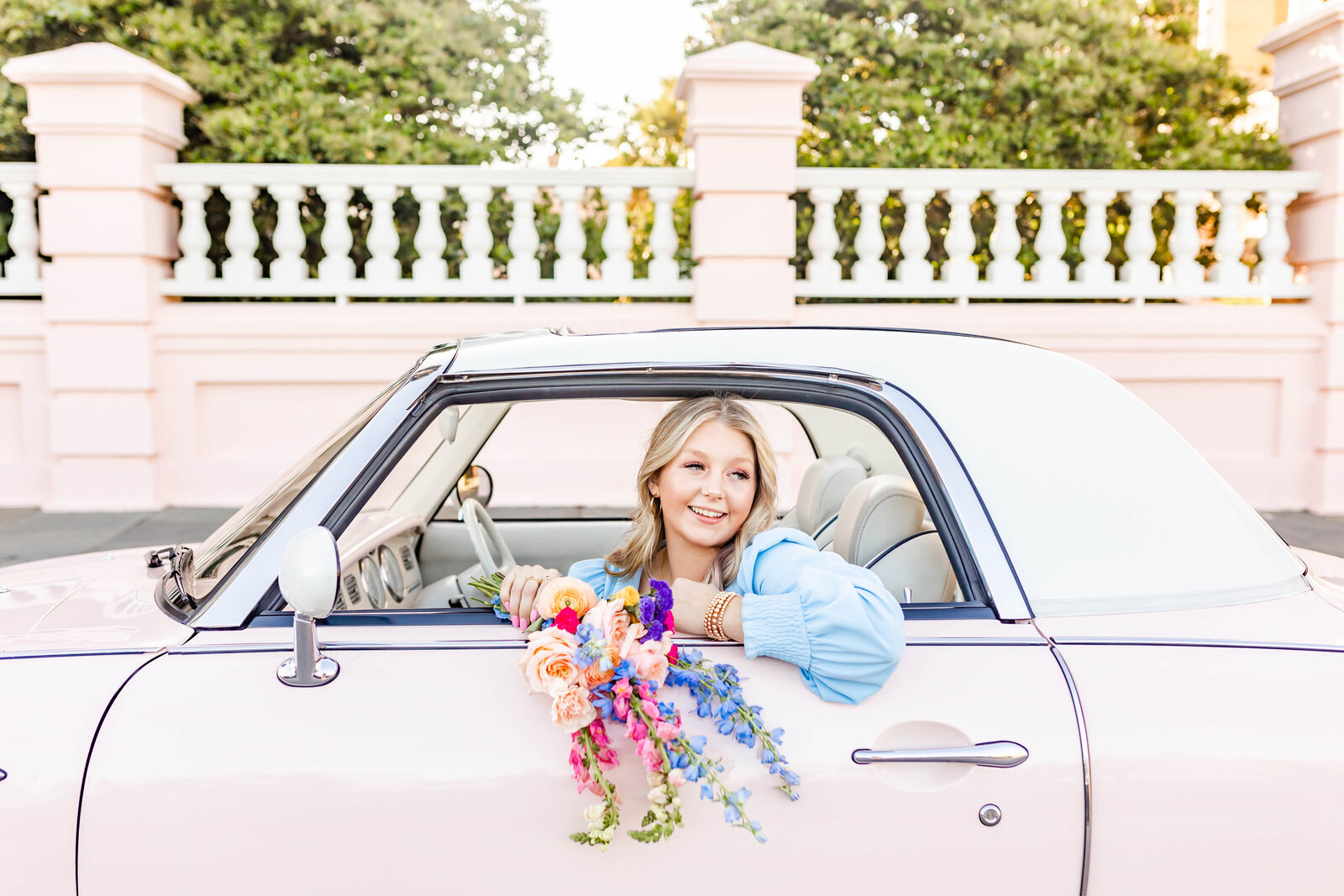 senior girl in blue dress with flowers in pink car on Charleston waterfront