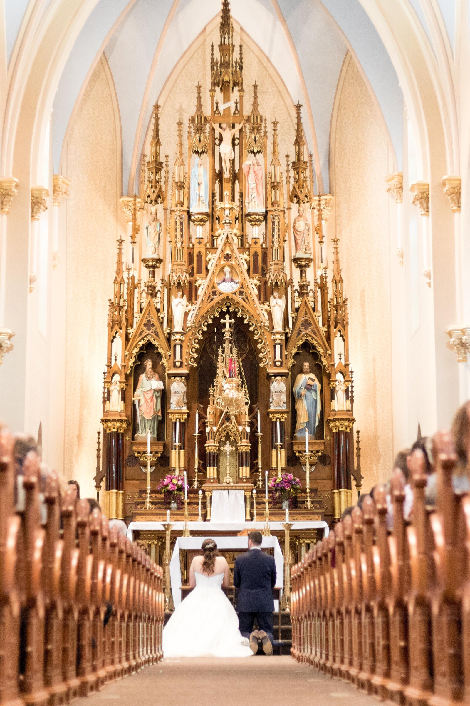 bride and groom kneel at front of majestic Catholic church