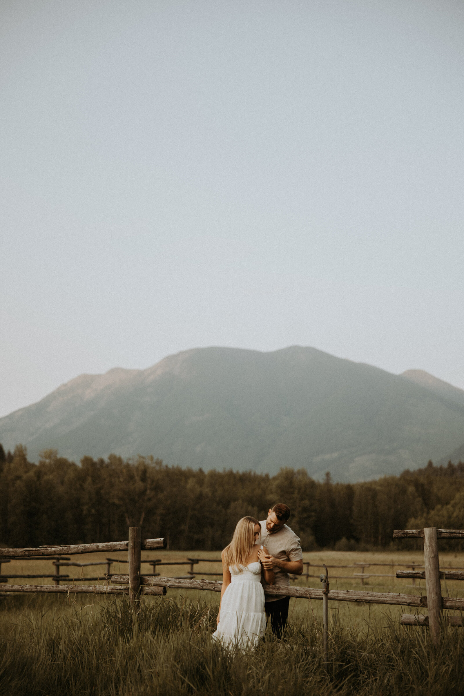 photo of couple sitting up against a fence during their montana engagement photos 